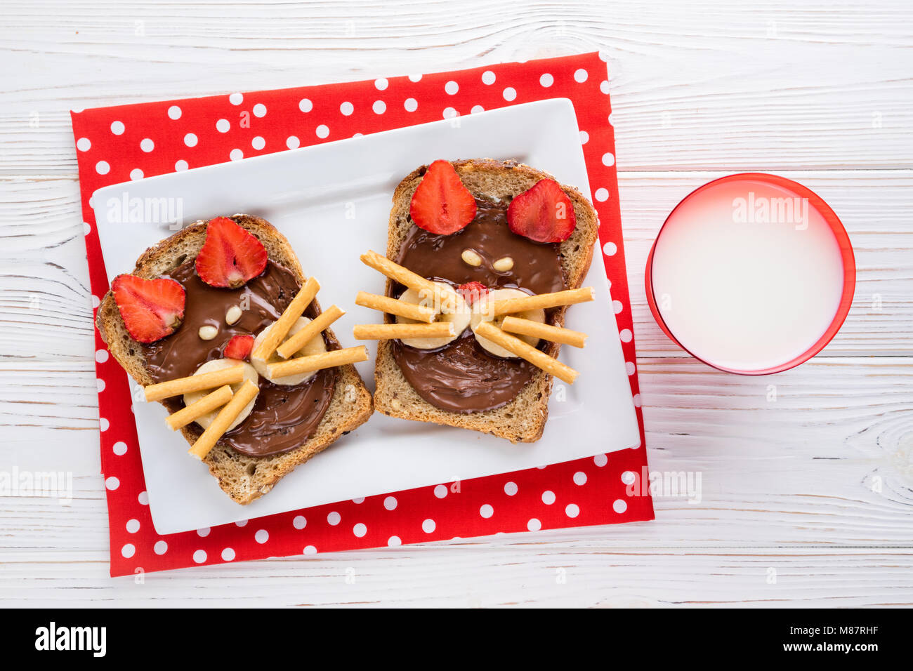 Sandwiches und Milch für die Kinder. Lustige Katzen Gesicht Sandwiches mit Beeren, Schokolade, Bananen, Nüsse. Ansicht von oben Stockfoto