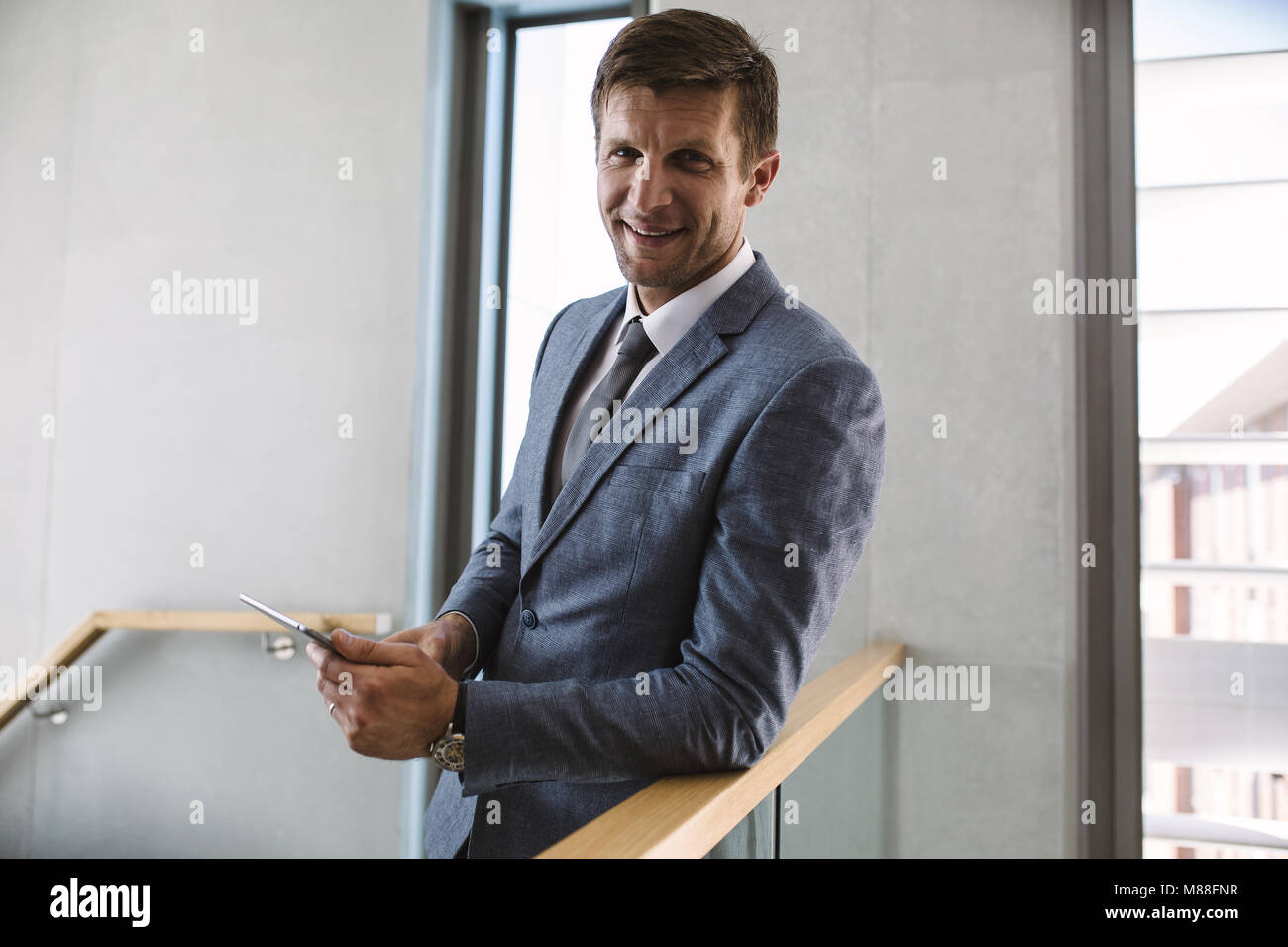 Portrait von Happy Geschäftsmann, stehen im Büro Flur mit einem digitalen Tablet. Männliche Unternehmer an Kamera suchen und lächelnd. Stockfoto