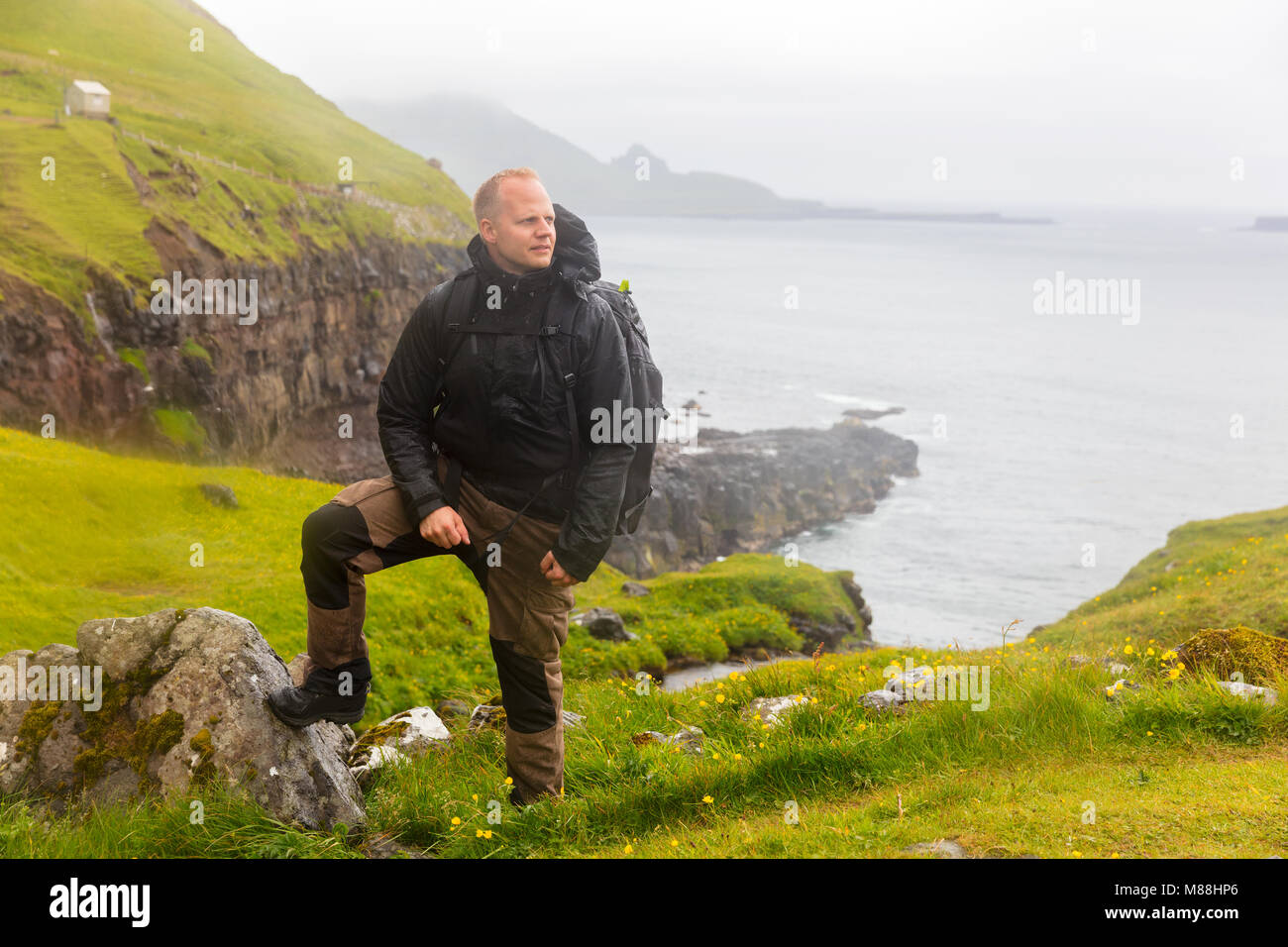 Wanderer im Regen stehen auf dem Berg auf den Färöer Insel mit Blick auf das Meer im Hintergrund Stockfoto