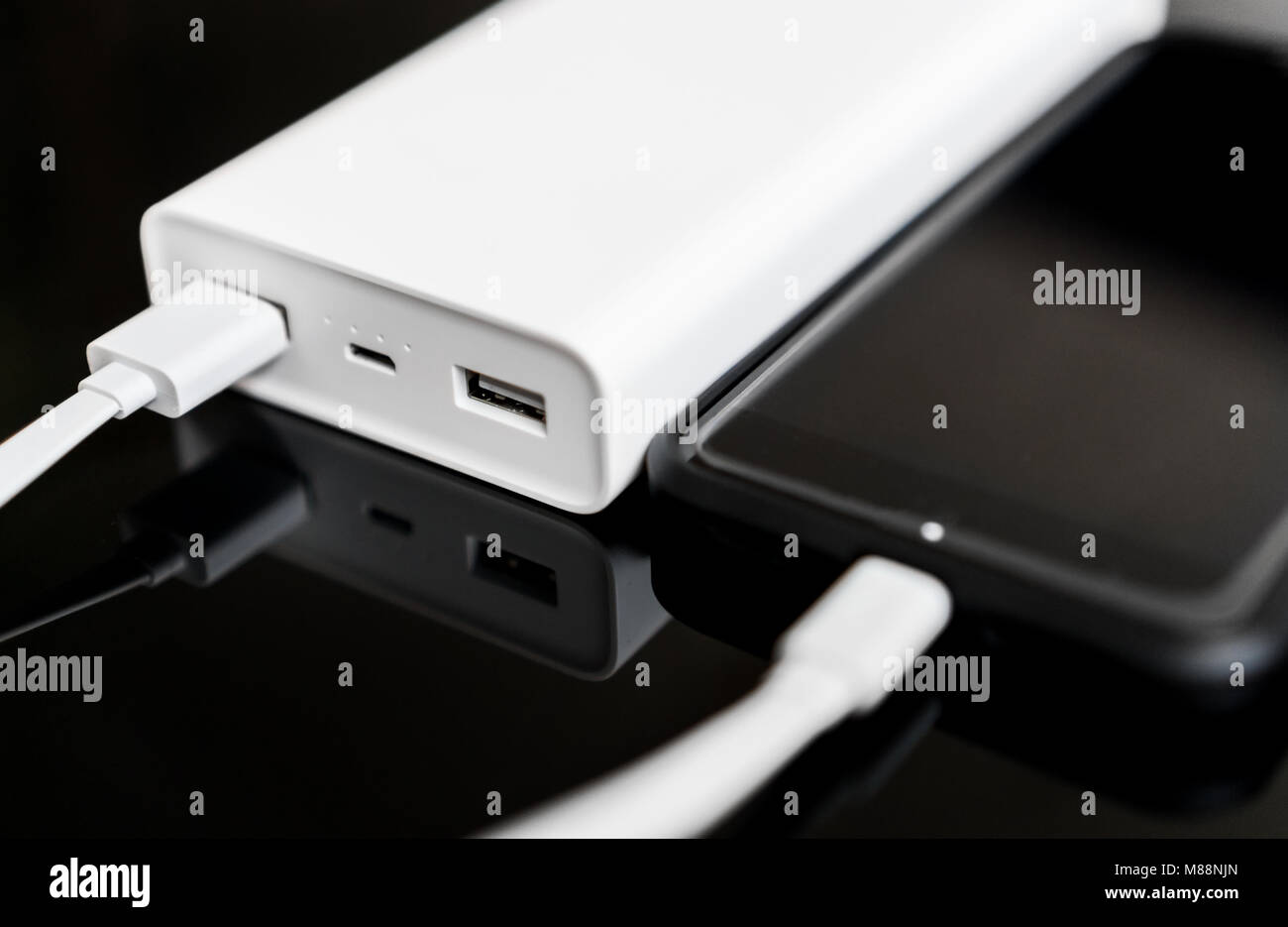 White Power Bank mit Smartphone auf verspiegelte Oberfläche. Stockfoto