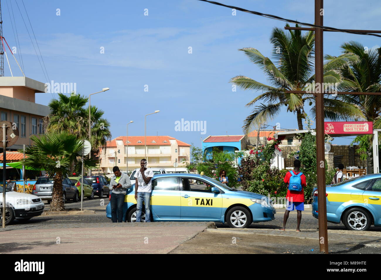 Ein Taxifahrer lehnt sich gegen sein Auto beim Warten auf Kunden, im Zentrum von Santa Maria auf der Insel Sal, Kapverden. Stockfoto