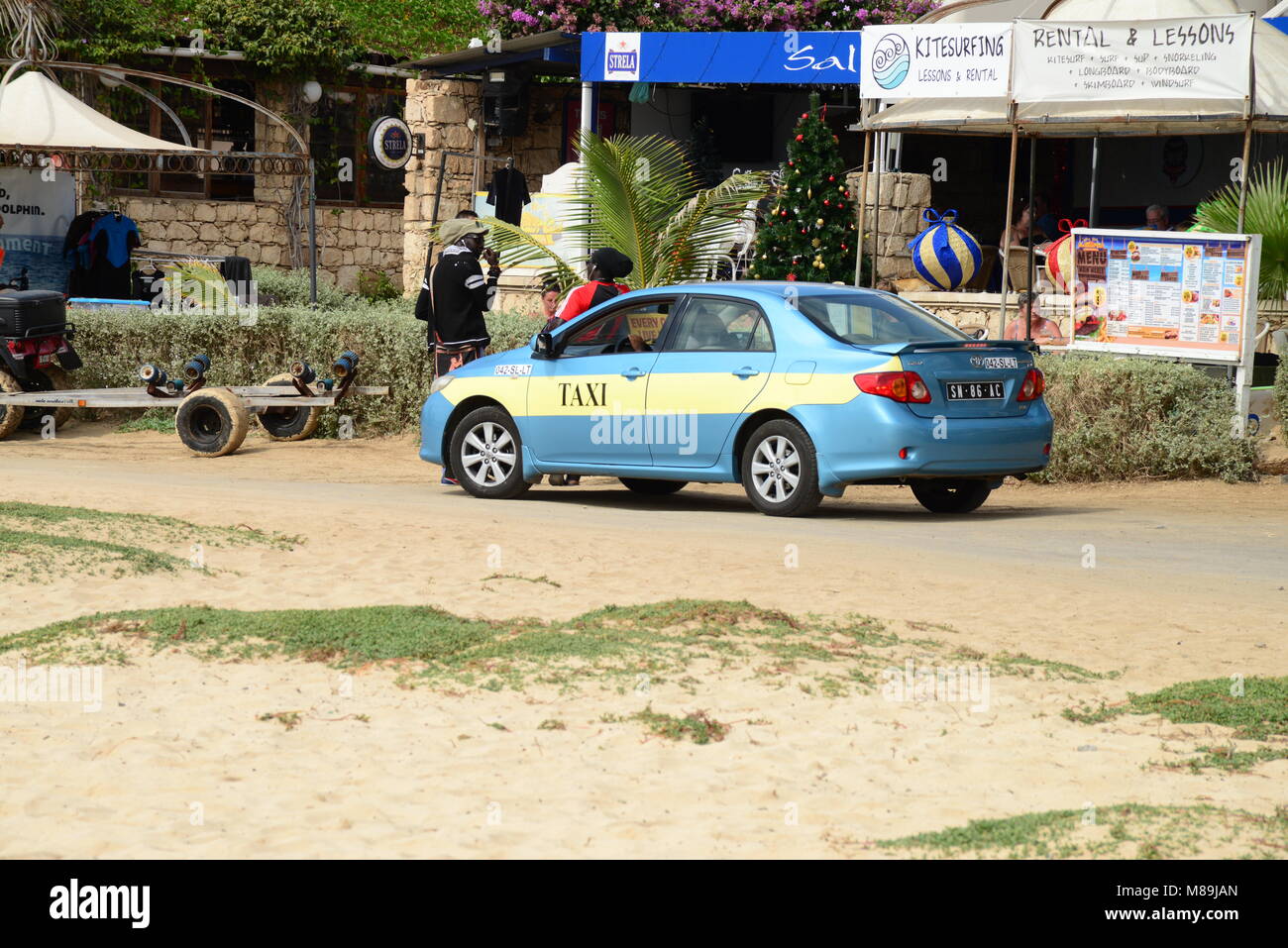 Taxifahrer Gespräche mit einem Freund und lehnt sich auf seinem Auto in der Nähe vom Strand geparkt - front Cafe im Zentrum von Santa Maria, Insel Sal, Kap Verde (Afrika). Stockfoto