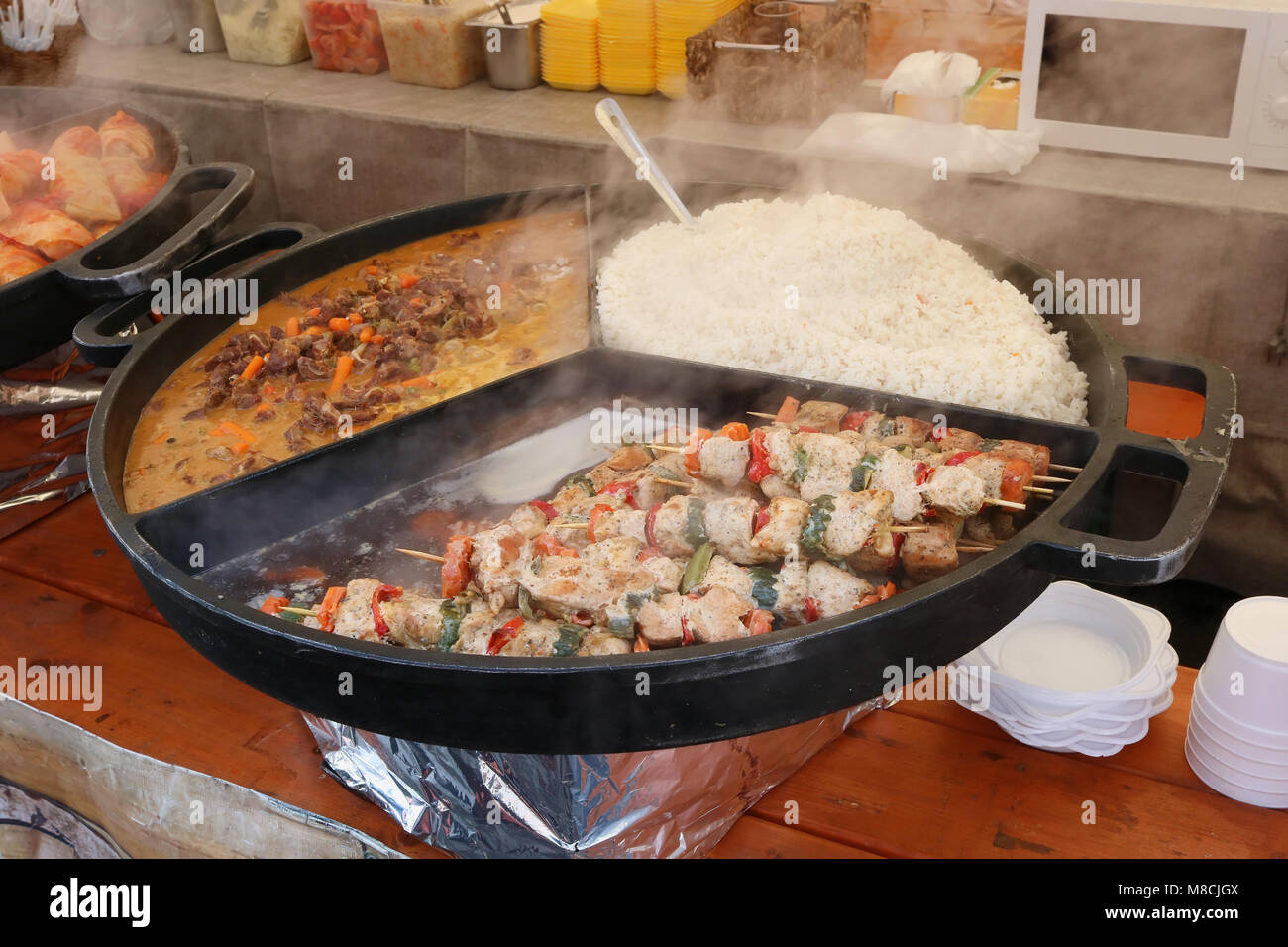 Straße fast food - gekochten Reis, Rind Fleisch mit Chili Sauce und gebratenes Schweinefleisch auf Holzspieße auf einem großen Stahl Bratpfanne. Frühling März Tag ou Stockfoto