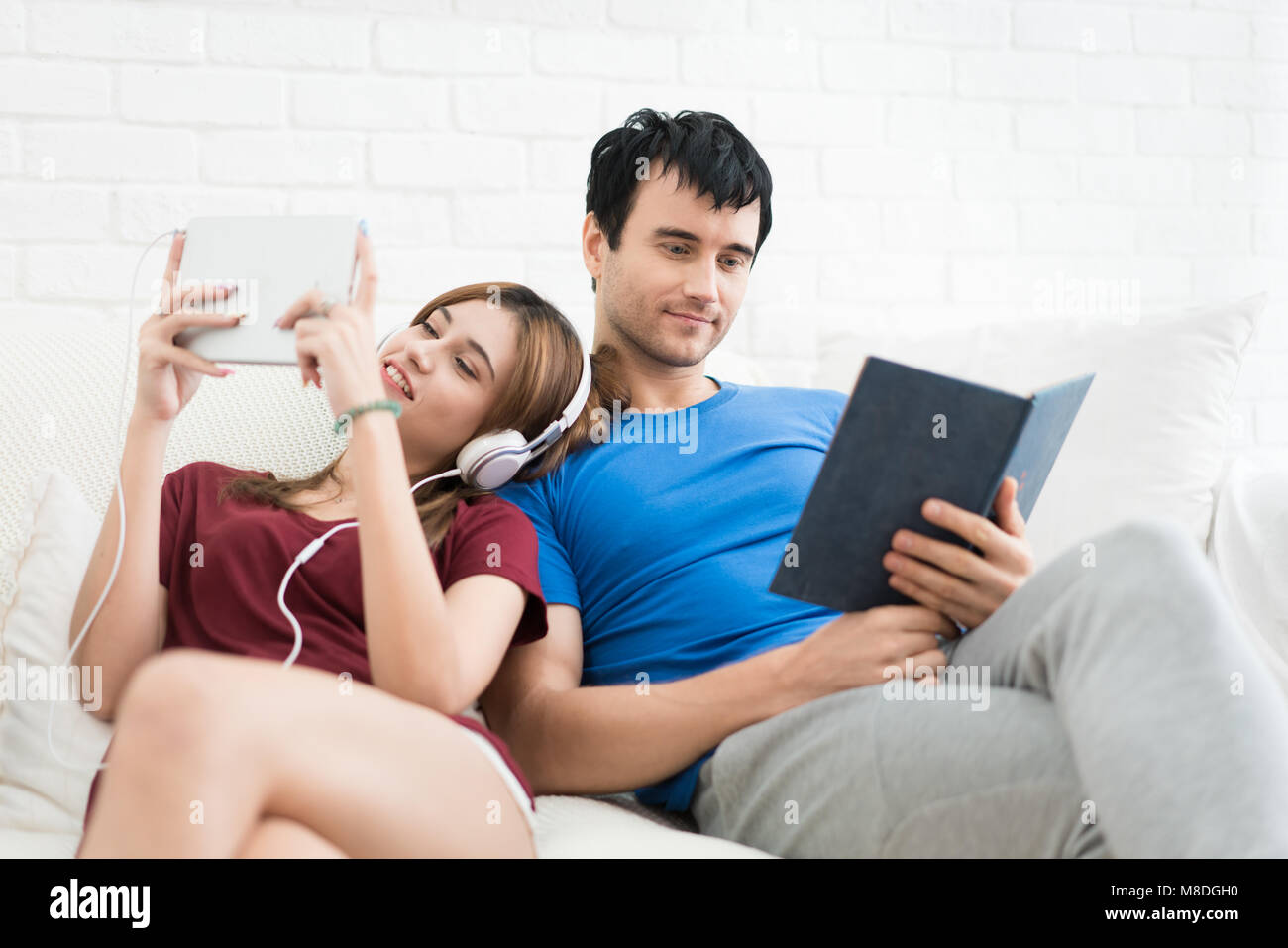 Junges Paar auf dem Sofa entspannen in Ihrem Wohnzimmer zu Hause. Musik hören und lesen ein Buch. Stockfoto