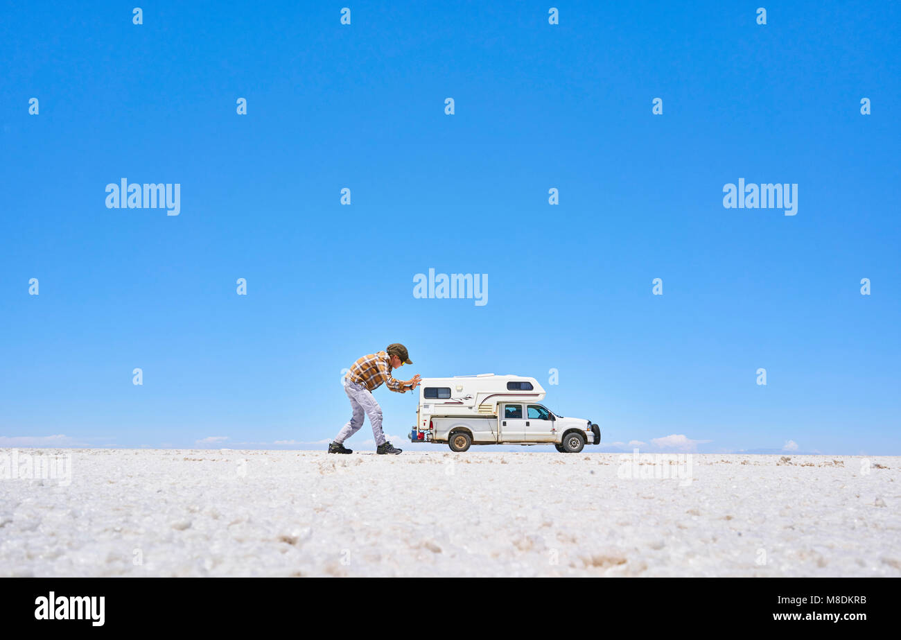 Falschen Perspektive Bild der Junge auf Salt Flats, vortäuschen, das Fahrzeug zu schieben, Fahrzeug im Hintergrund, Salar de Uyuni, Oruro, Bolivien Stockfoto