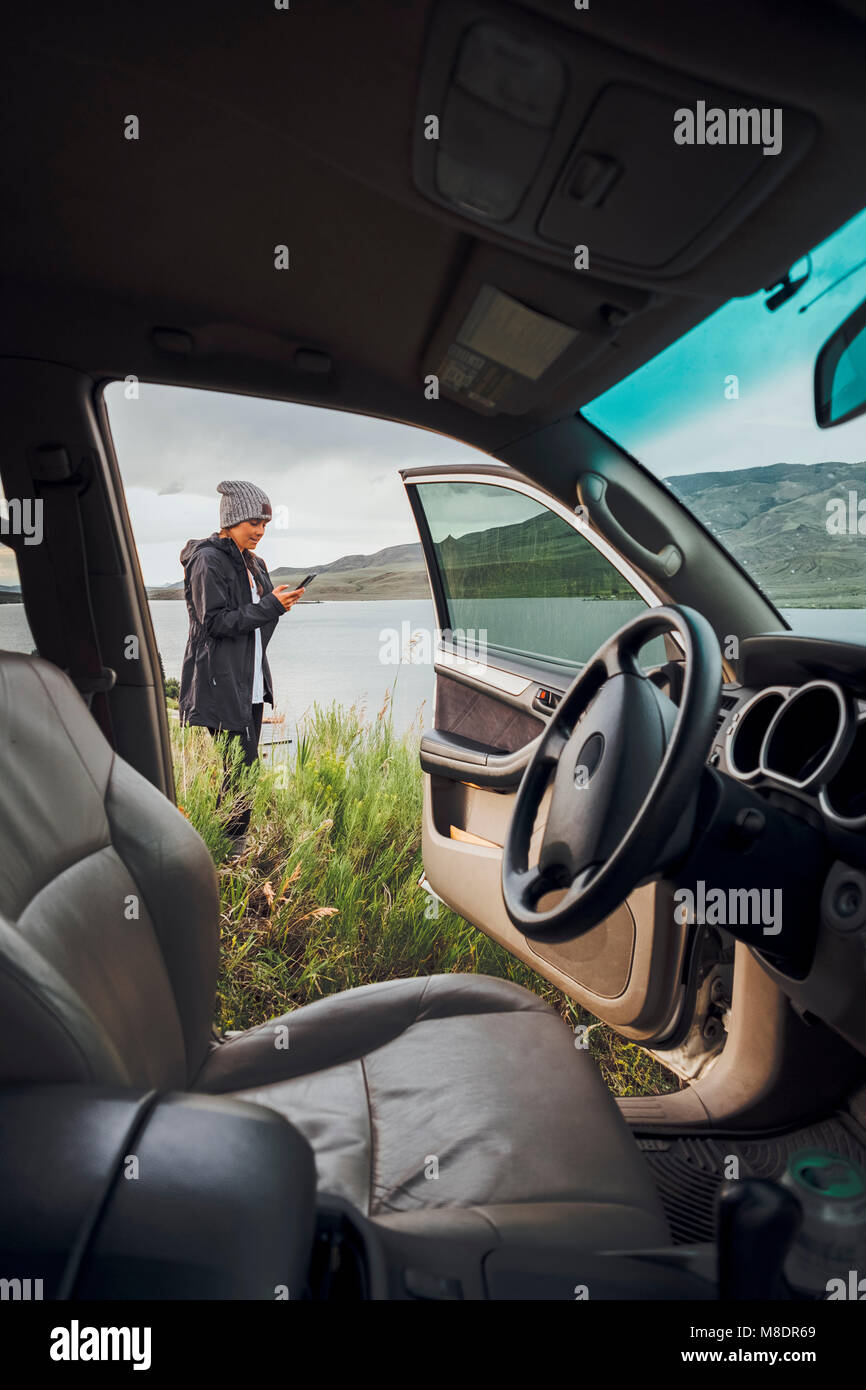 Junge Frau stand neben Dillon Reservoir, Smartphone, Blick durch die geparkten Auto, Silverthorne, Colorado, USA Stockfoto