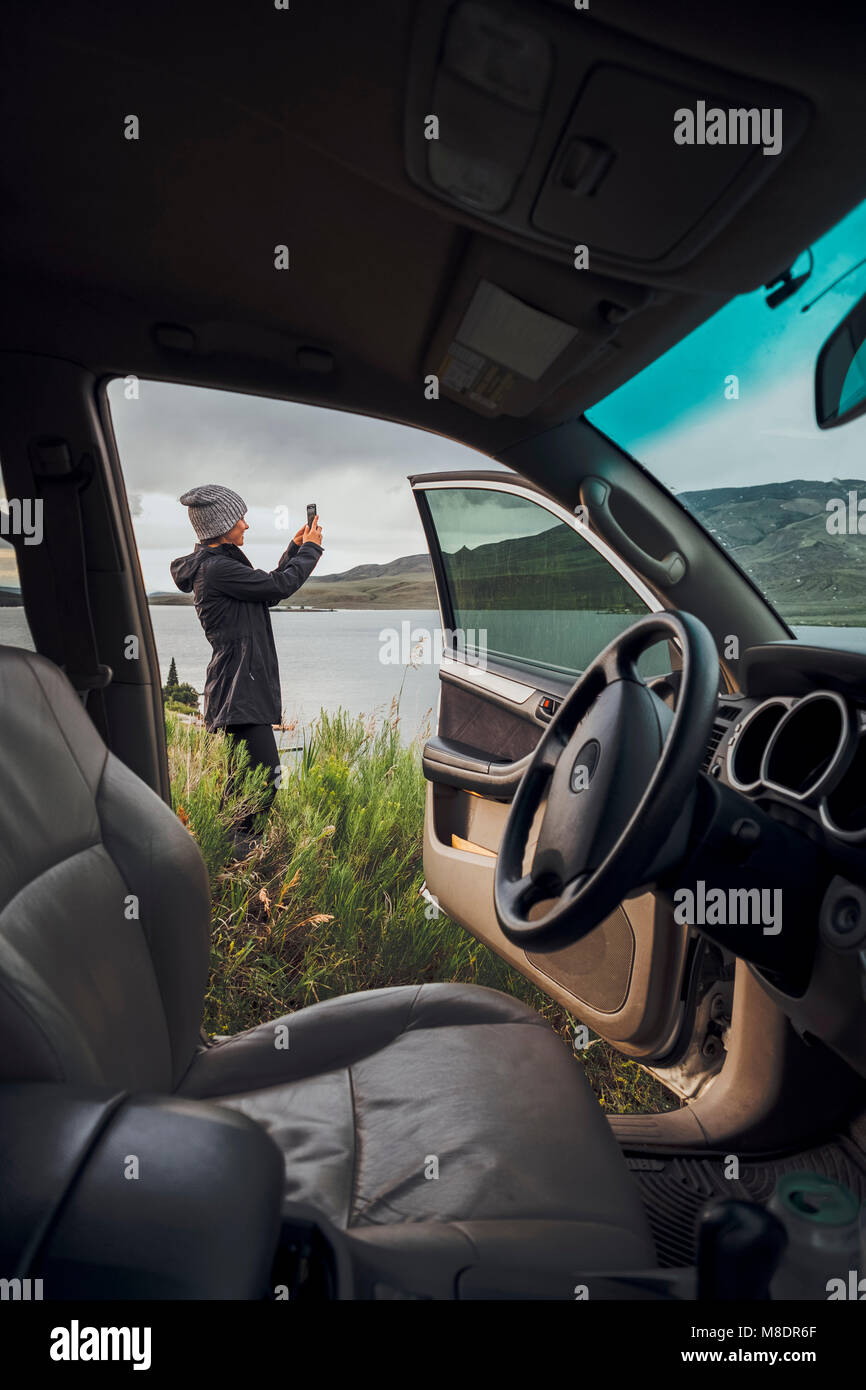 Junge Frau stand neben Dillon Reservoir, Smartphone, Blick durch die geparkten Auto, Silverthorne, Colorado, USA Stockfoto