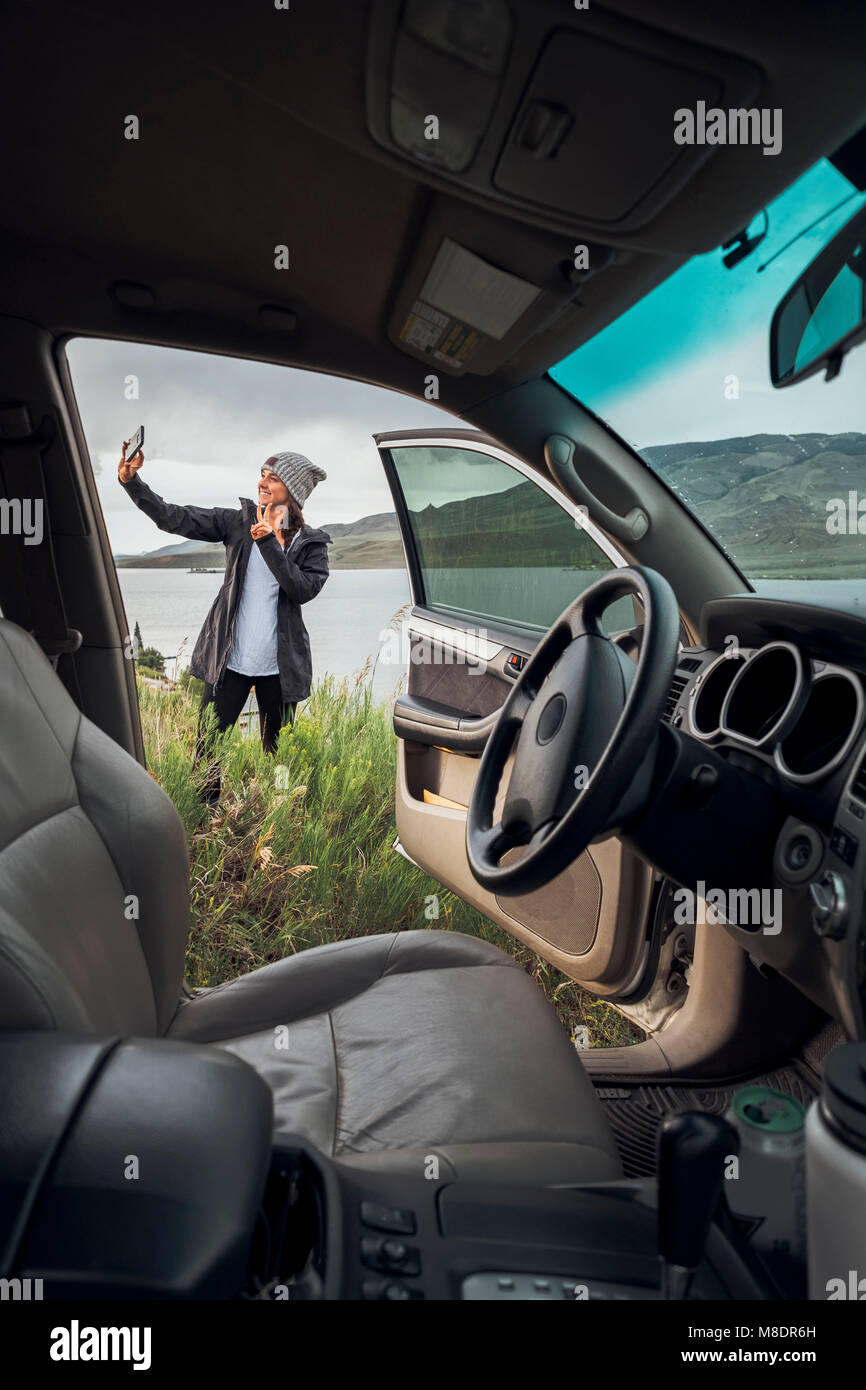 Junge Frau stand neben Dillon Reservoir, Smartphone, Blick durch die geparkten Auto, Silverthorne, Colorado, USA Stockfoto