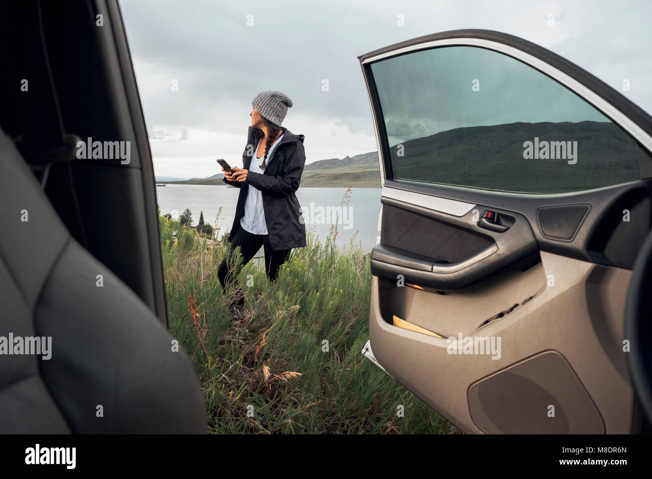 Junge Frau stand neben Dillon Reservoir, Smartphone, Blick durch die geparkten Auto, Silverthorne, Colorado, USA Stockfoto