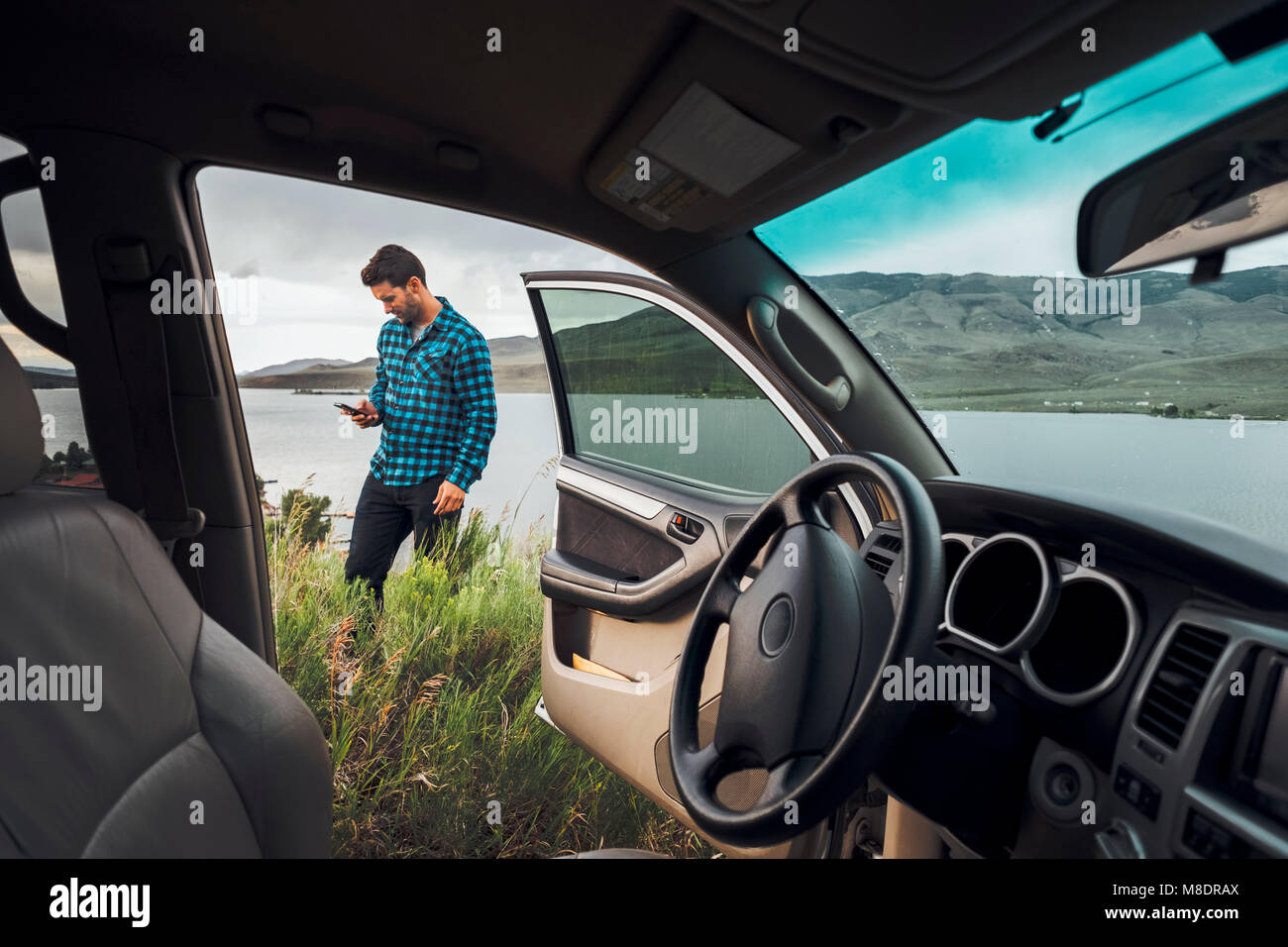 Mitte der erwachsene Mann stand neben Dillon Reservoir, Smartphone, Blick durch die geparkten Auto, Silverthorne, Colorado, USA Stockfoto