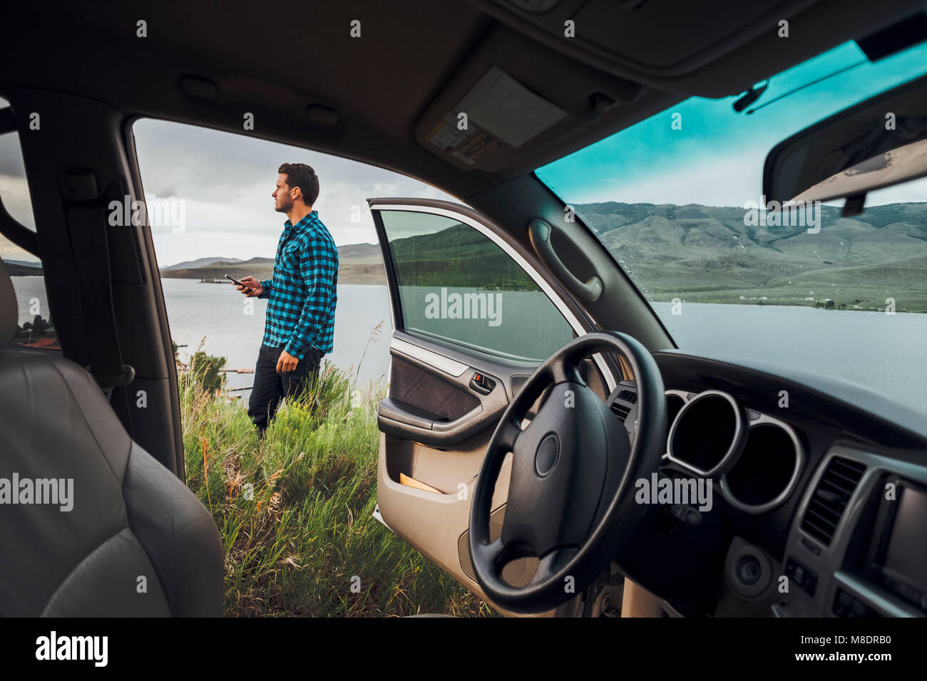 Mitte der erwachsene Mann stand neben Dillon Reservoir, Smartphone, Blick durch die geparkten Auto, Silverthorne, Colorado, USA Stockfoto
