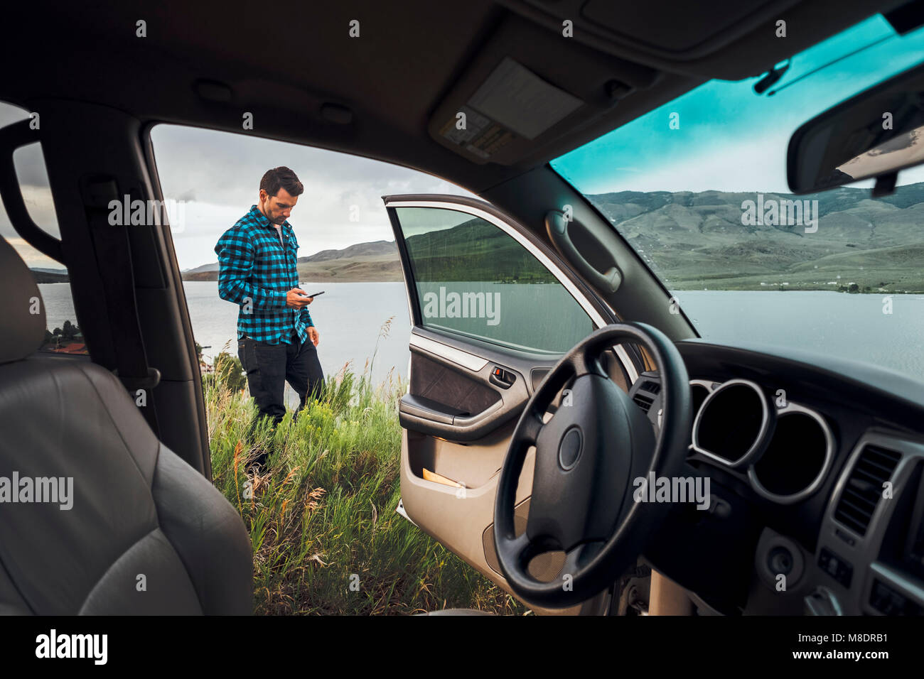 Mitte der erwachsene Mann stand neben Dillon Reservoir, Smartphone, Blick durch die geparkten Auto, Silverthorne, Colorado, USA Stockfoto