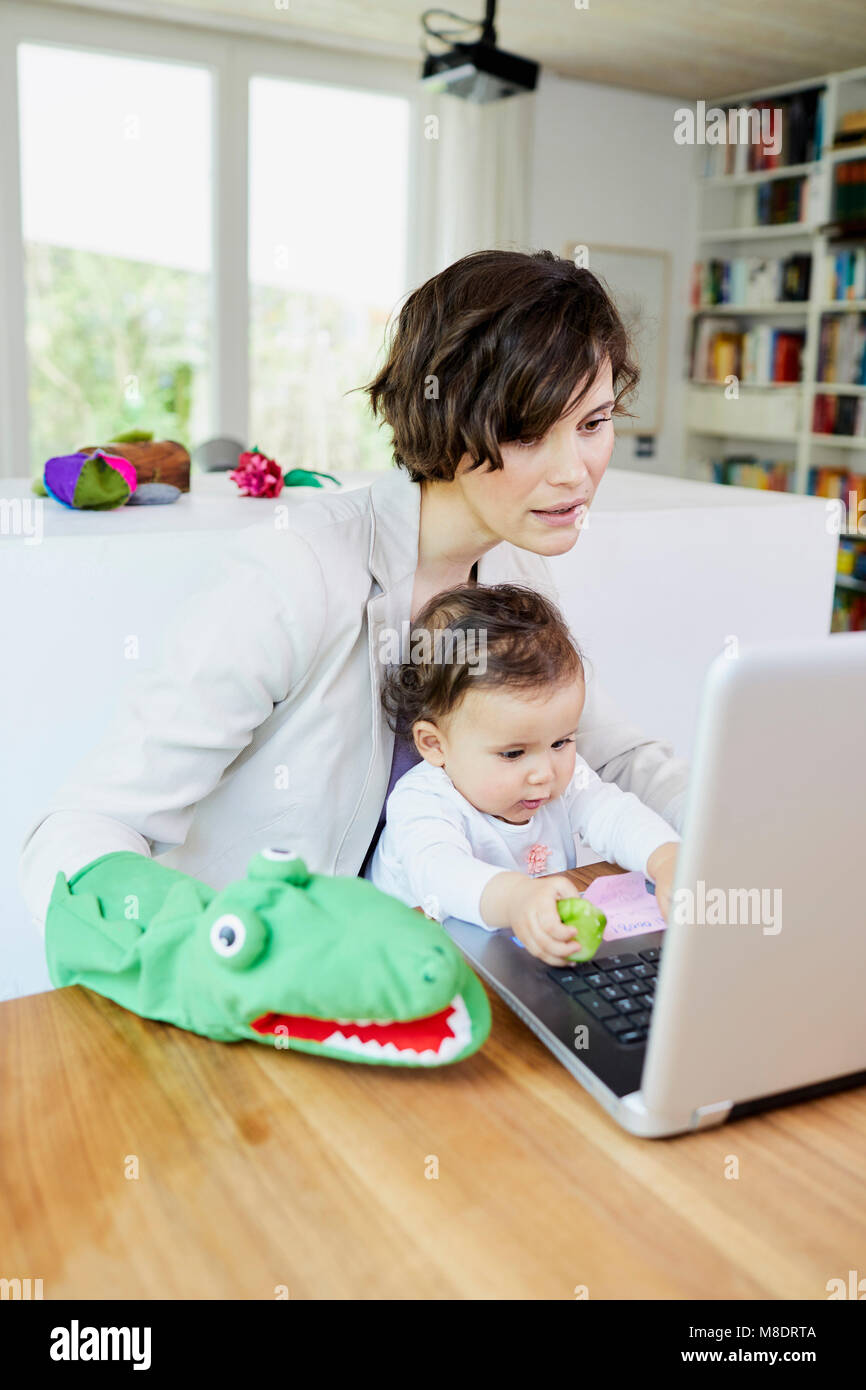 Mutter mit Laptop mit Baby Mädchen sitzen auf dem Schoß Stockfoto