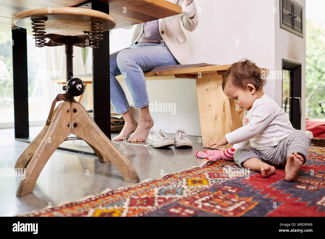 Mutter am Küchentisch arbeiten, während Baby Mädchen spielt auf dem Boden. niedrige Abschnitt Stockfoto
