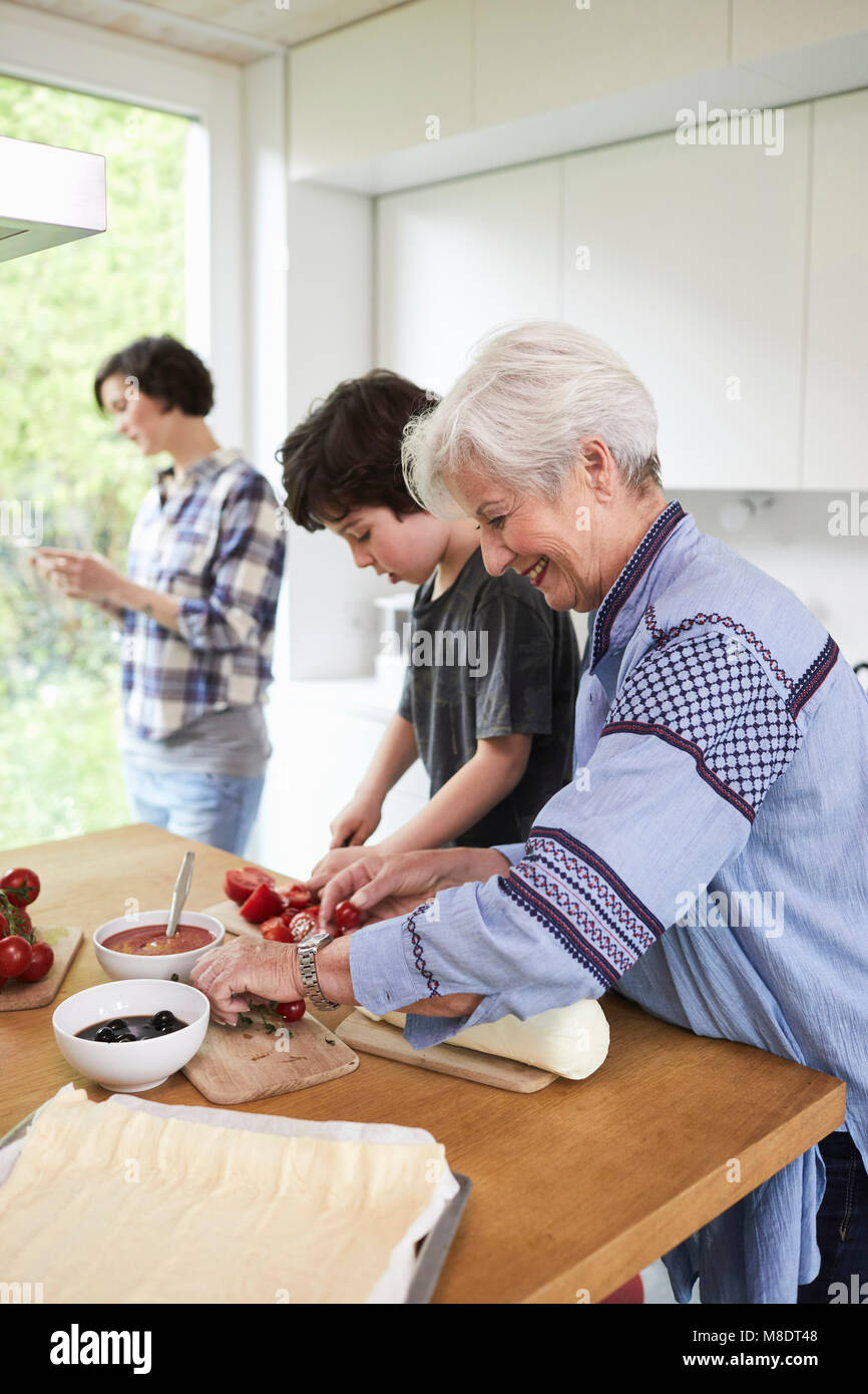 Großmutter und Enkel die Zubereitung von Speisen in der Küche, die Mutter im Hintergrund Stockfoto