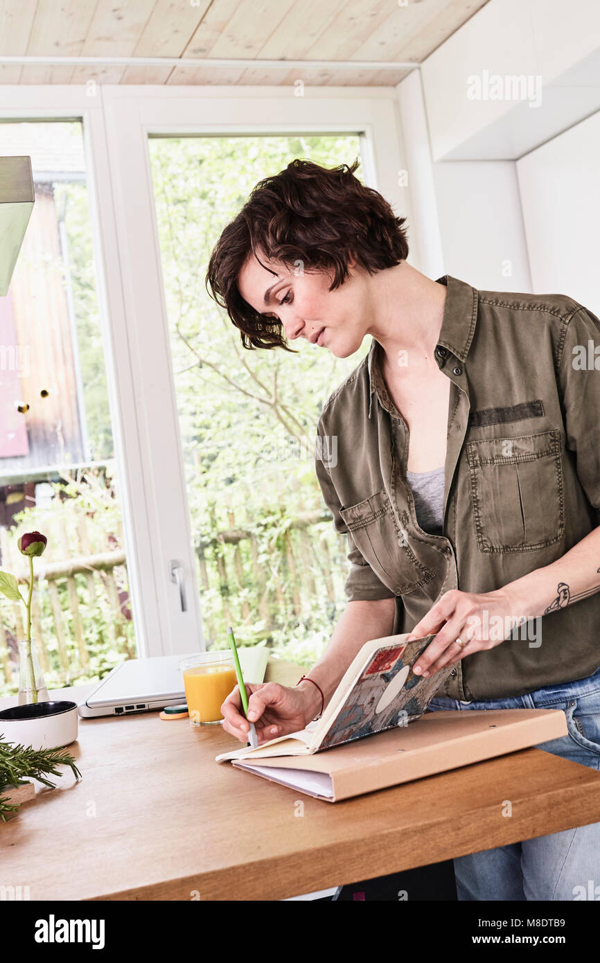 Mitte der erwachsenen Frau zu Hause, Schreiben in Buch Stockfoto