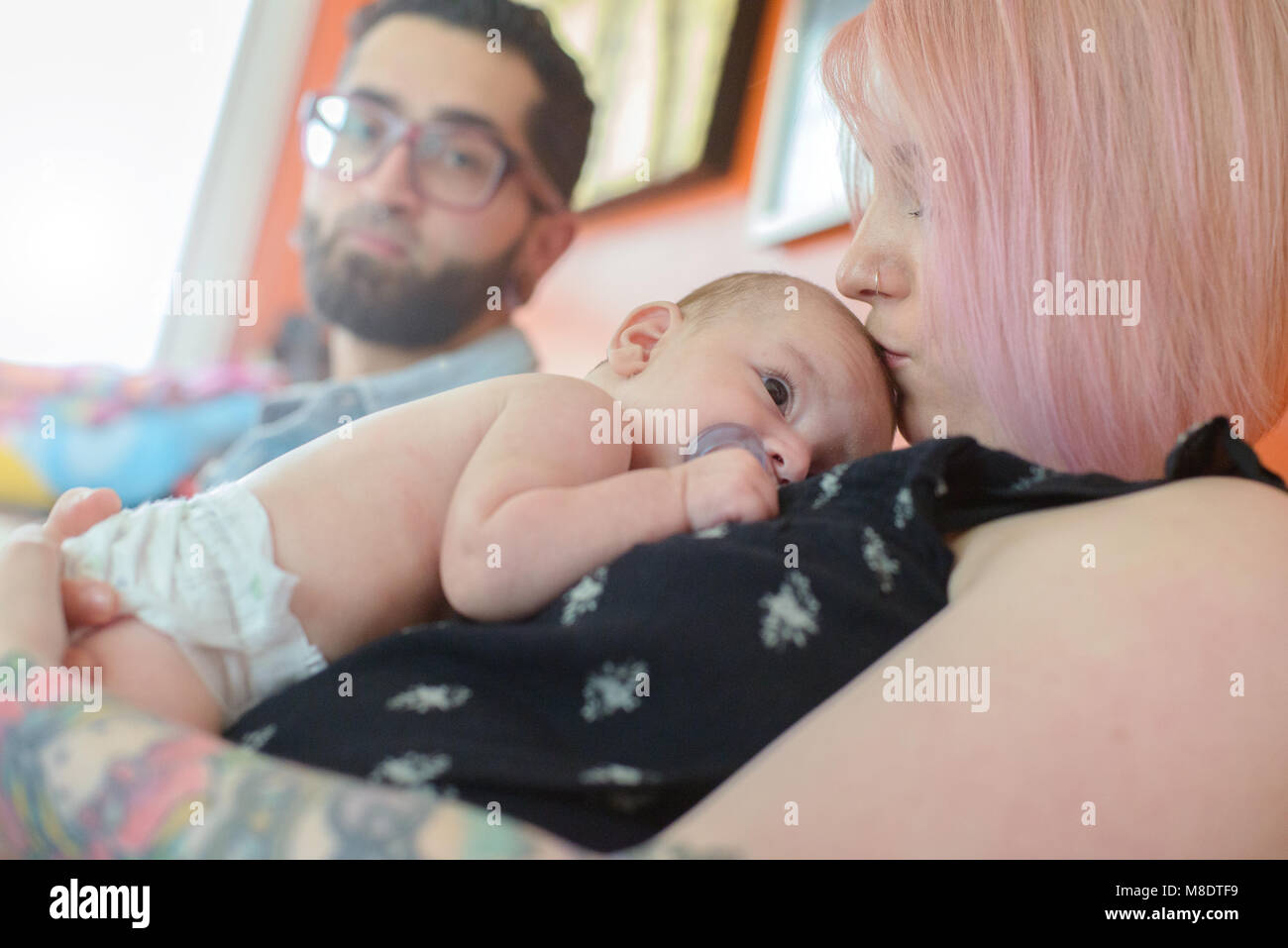 Frau mit Baby auf Brust, der Mann im Hintergrund Stockfoto