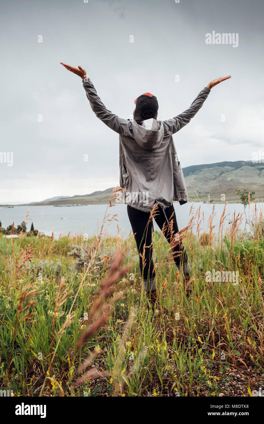 Junge Frau, die in der Nähe von Dillon Reservoir, Arme angehoben, Rückansicht, Silverthorne, Colorado, USA Stockfoto