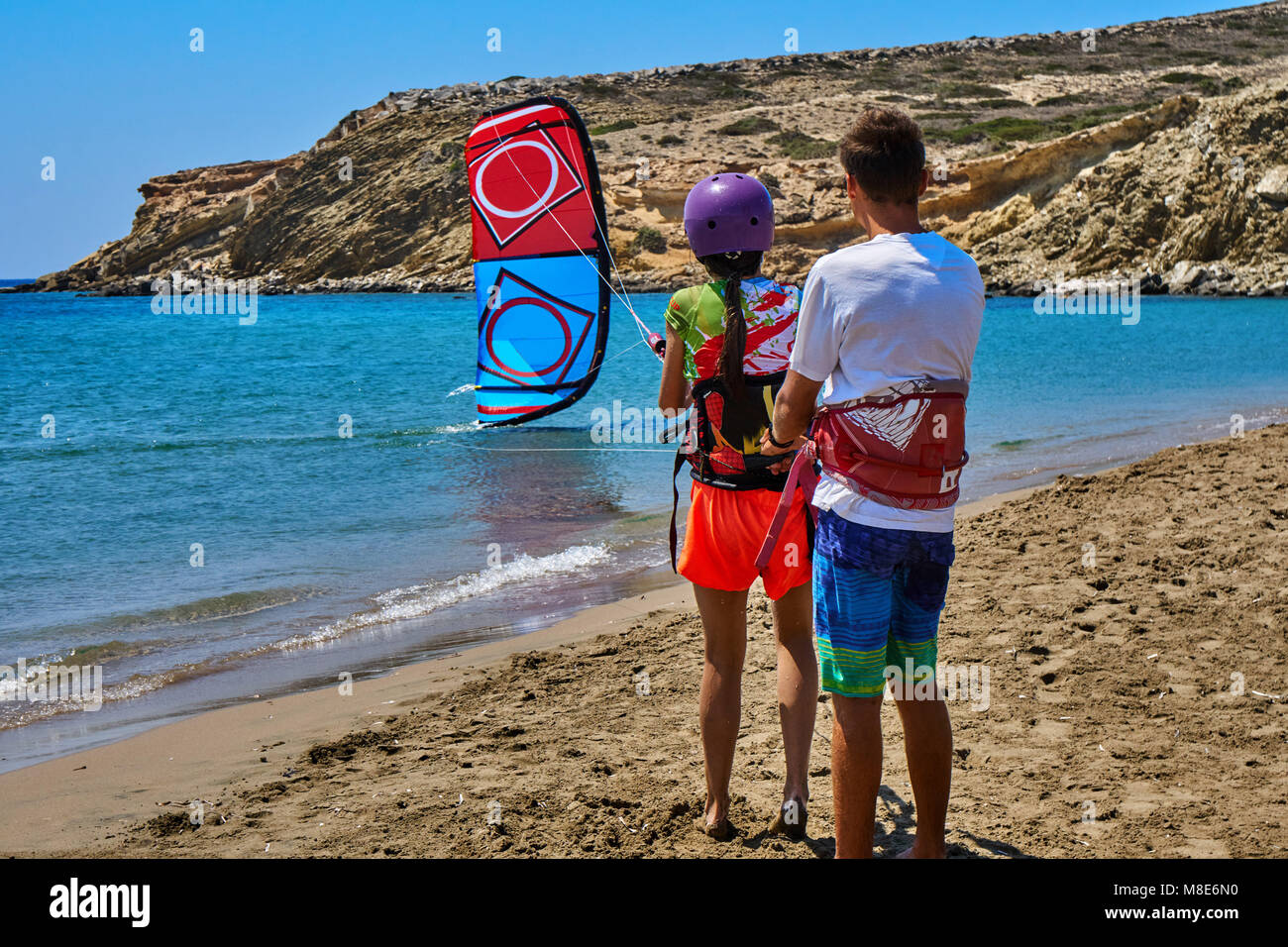 Die Trainerin lehrt junge Frauen, an einem sonnigen Sommertag auf der Rückseite am ruhigen Meeresstrand gegen den klaren Himmel Kitesurfen zu gehen Stockfoto