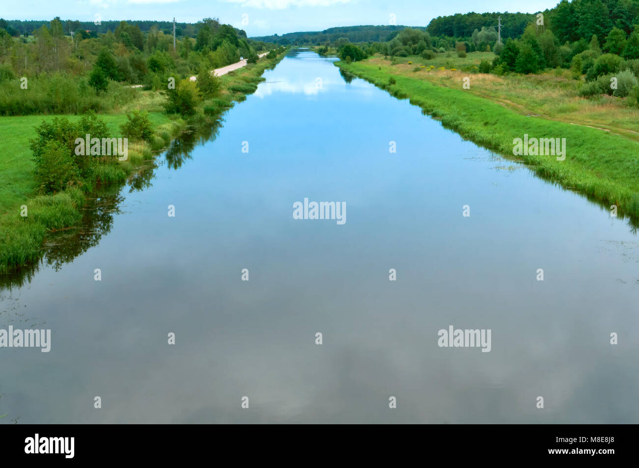 Glatten Kanal mit Reflexion des Himmels, langer Fluss mit bewachsenen grünen Ufern, künstlichen Teich Stockfoto