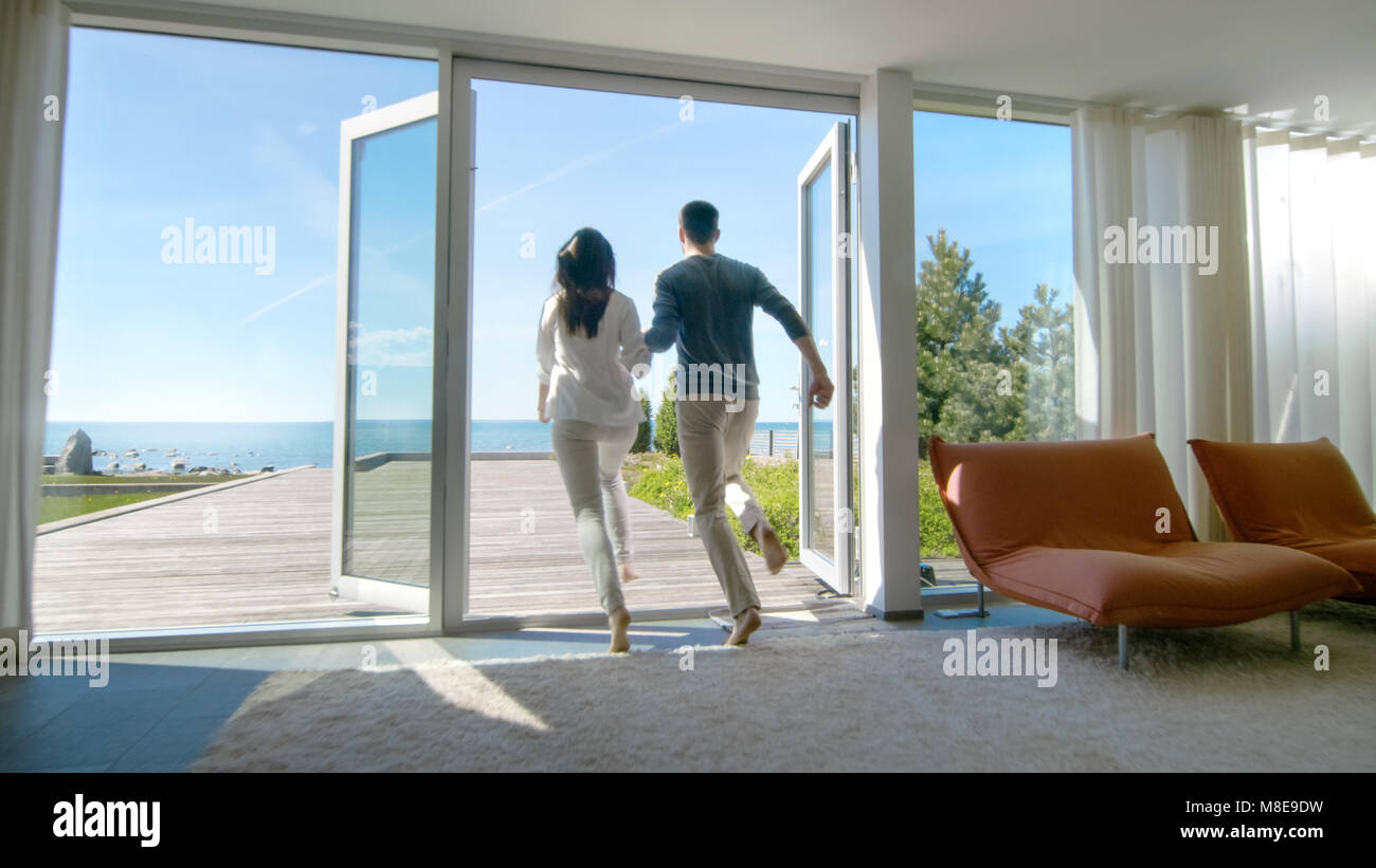 Glückliches Junges Paar Hand in Hand läuft aus Ihrem Haus auf der Terrasse mit Meerblick. Stockfoto