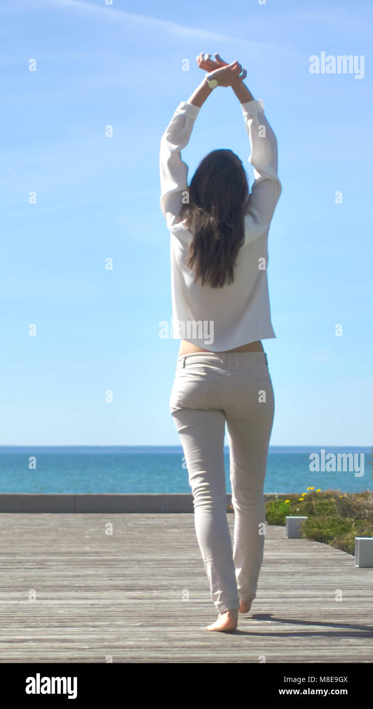 Schuss eine schöne Brünette mit losen Haare Öffnen von Türen auf den Balkon und Gehen auf die sonnige Terrasse mit Meerblick. Stockfoto