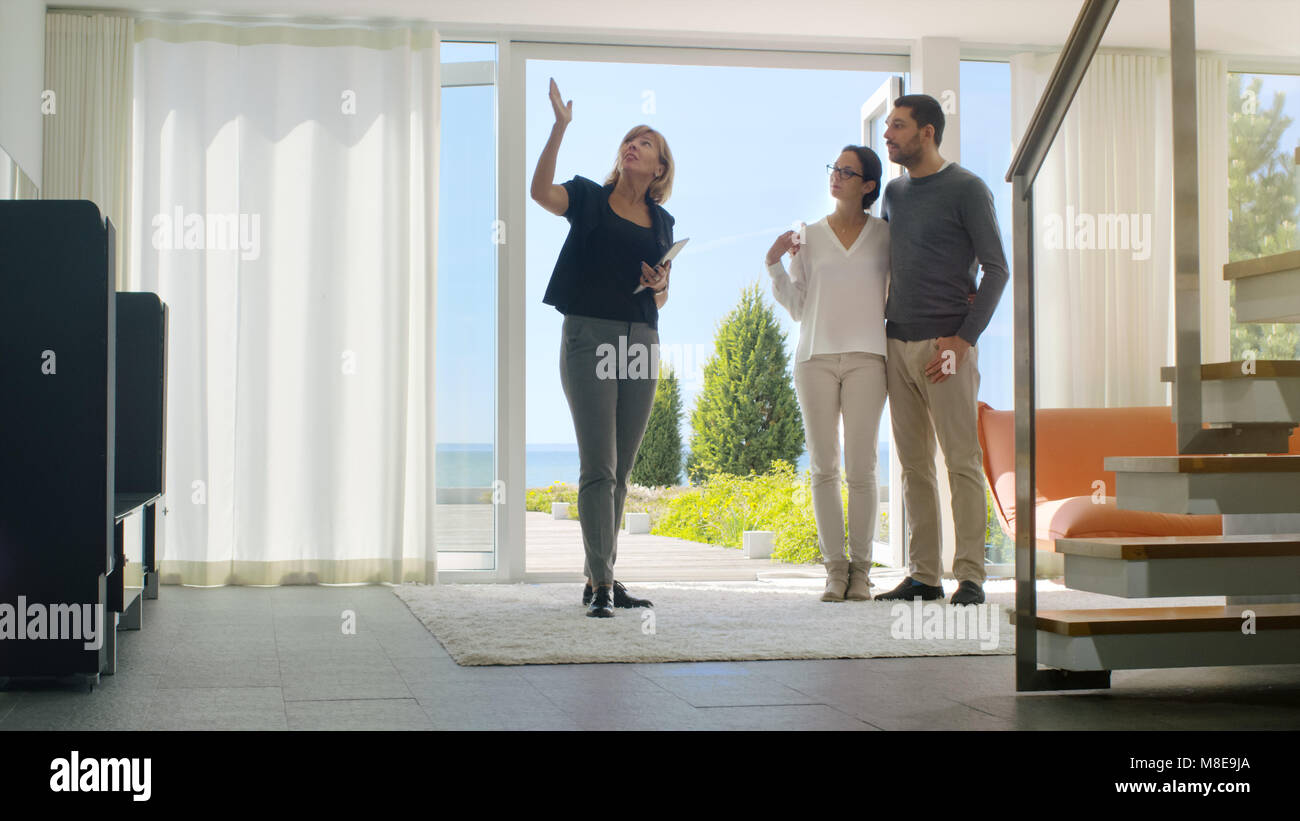 Professionelle Immobilien Agent zeigt ein stilvolles, modernes Haus mit einem schönen jungen Paar, das auf dem Markt für den Kauf/Miete neues Zuhause sind. Stockfoto