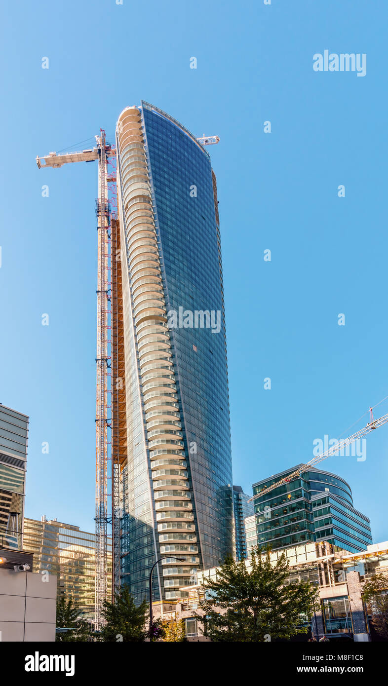 Der Aufbau einer modernen Wolkenkratzer mit einem Turm Kran und anderen Baumaschinen in der Stadt, neben Häusern und Gebäuden, Bäumen und anderen städtischen infr Stockfoto