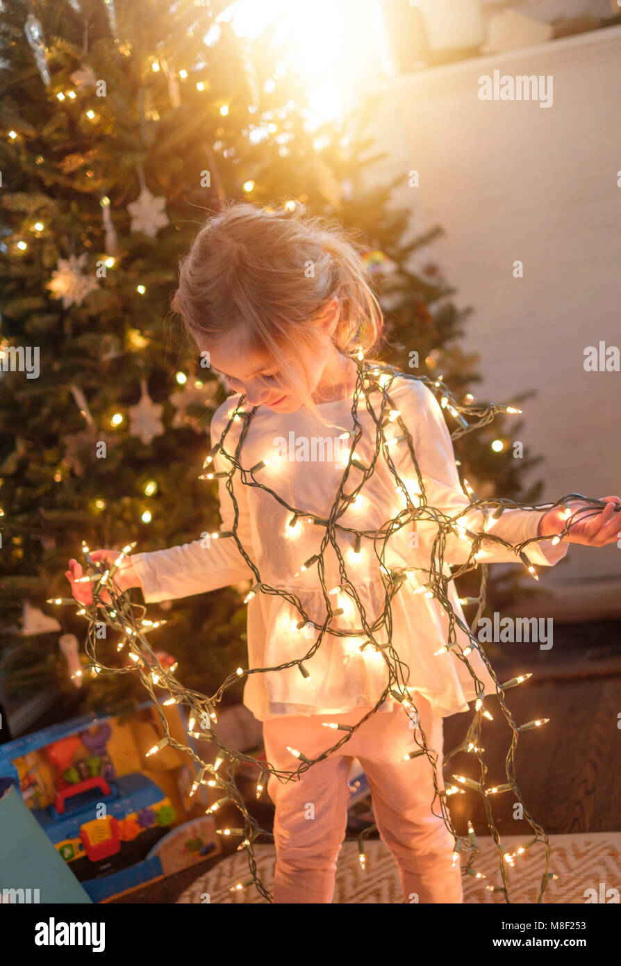 Kleines Mädchen (4-5) mit Weihnachtsbeleuchtung im Wohnzimmer gewickelt Stockfoto
