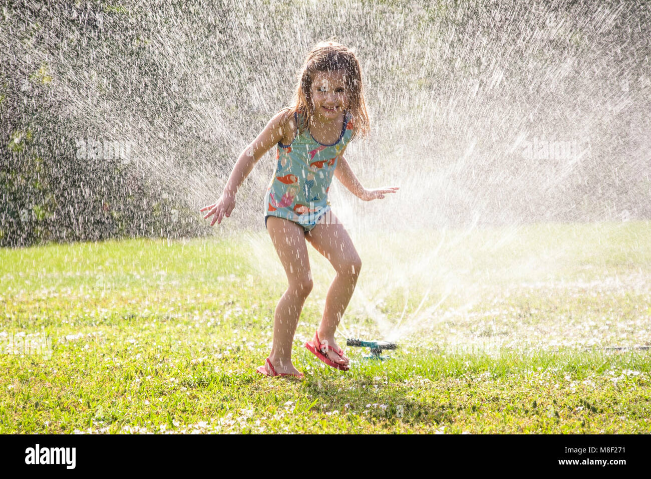 Mädchen (4-5) Spritzen in das Sprinklerwasser auf Rasen Stockfoto