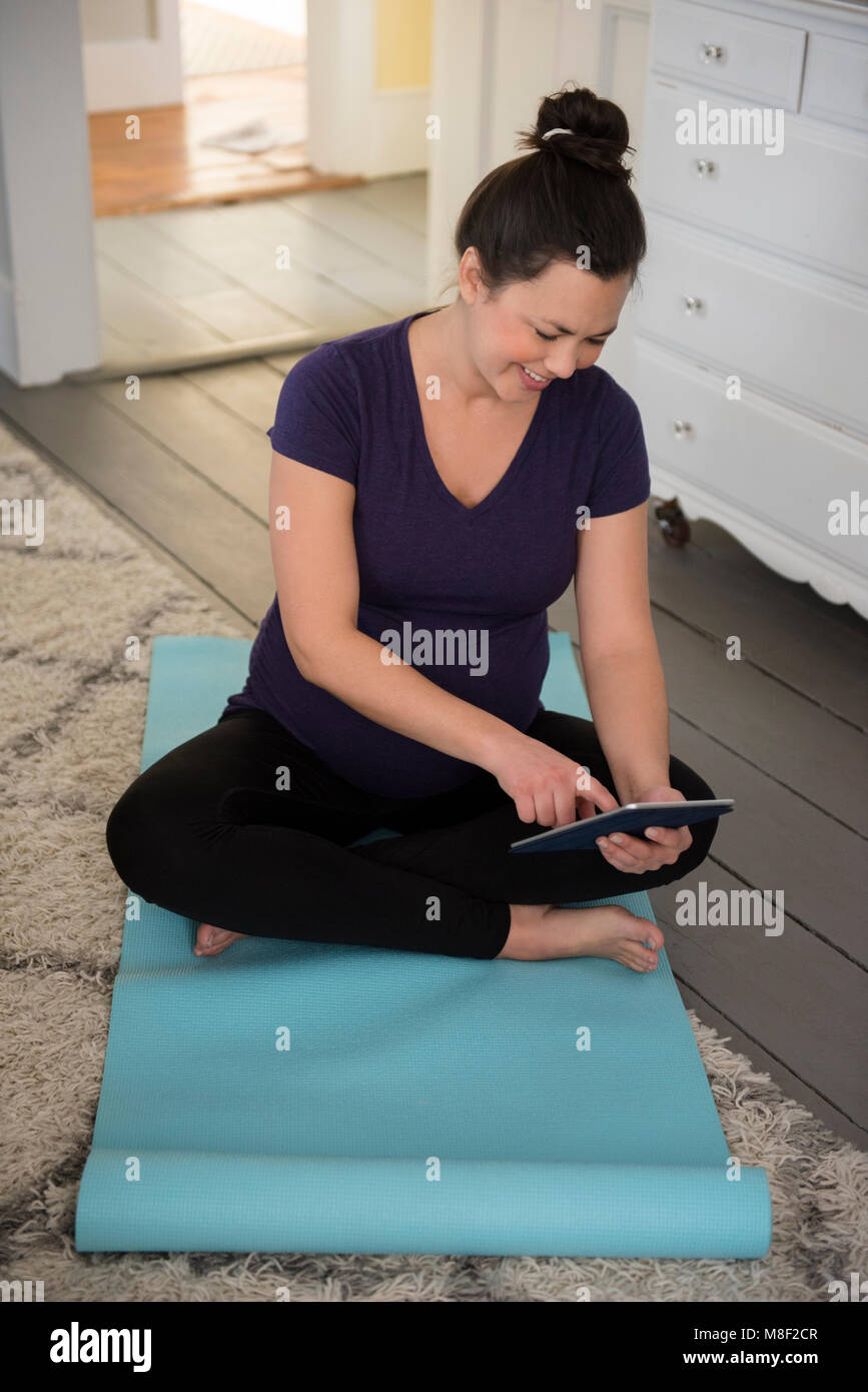 Schwangere Frau sitzt auf der Yogamatte und mit Tablet-PC Stockfoto