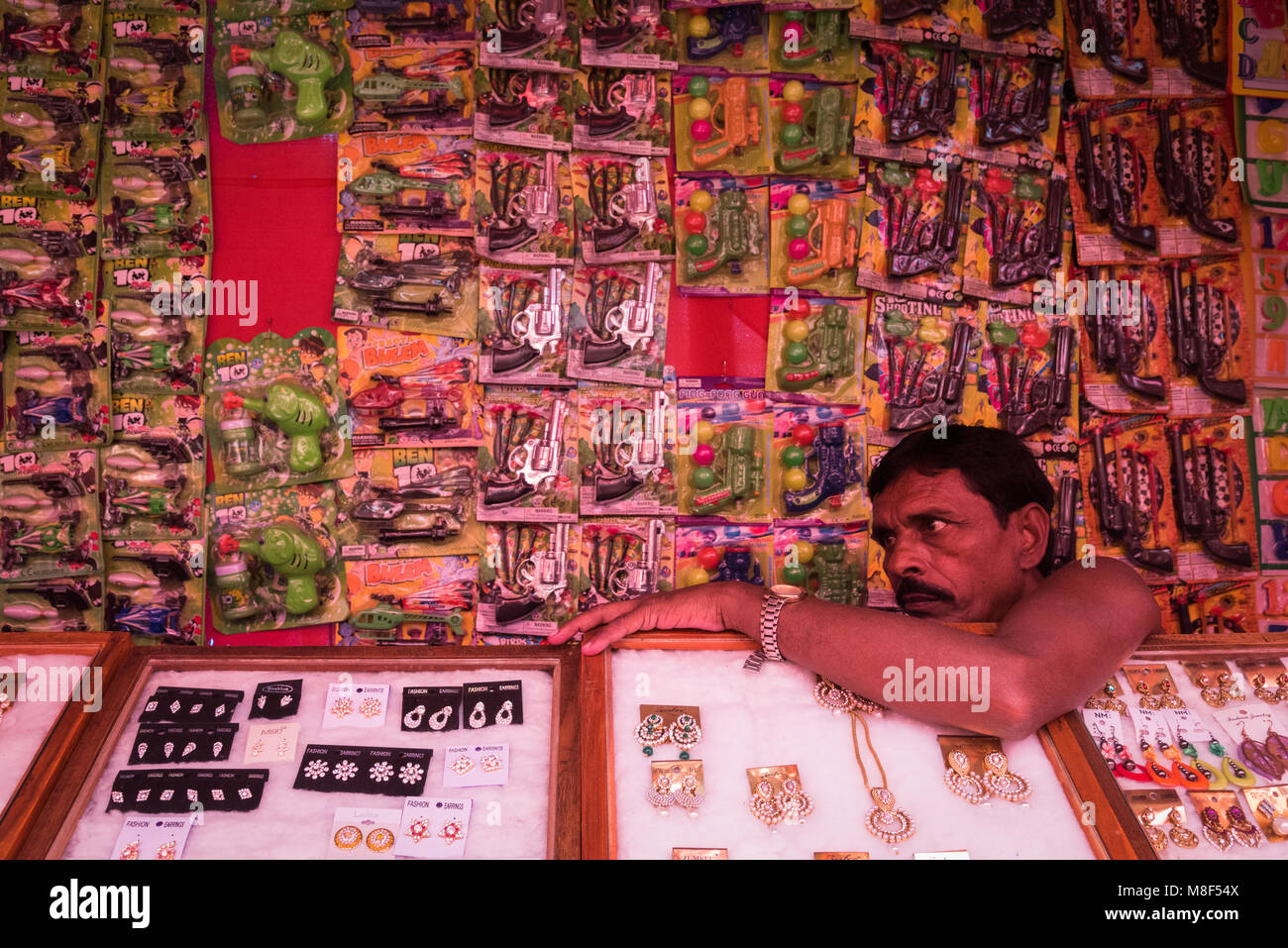 Ein Mann sitzt vor seiner Anzeige von spielzeugpistolen an der Sonepur Mela, Sonepur, Indien. Stockfoto