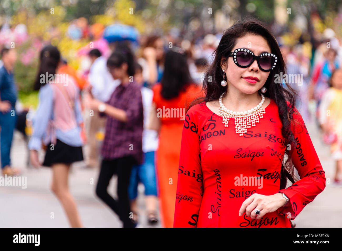 Ein Vietnam Frau im roten Kleid sagen, mehrfach aigon', und ein Paar von Gucci Sonnenbrillen, Ho Chi Minh City, Vietnam Stockfoto