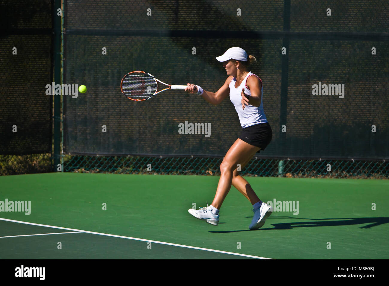 Anna Tatishvili in weißem Hemd und schwarzer Rock hits Tennis ball mit Schläger an sonnigen Green Court. Stockfoto