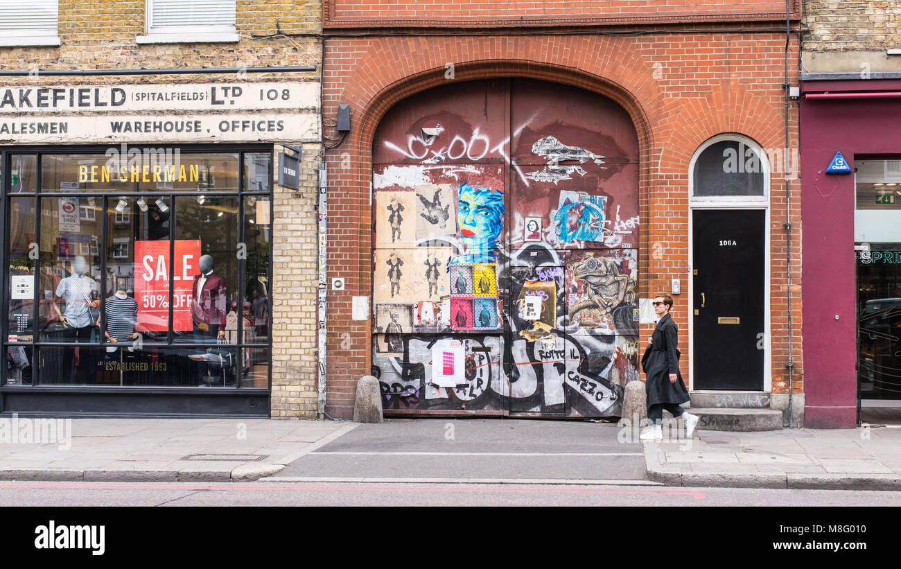 Coole hipster Frau vor eine alte Tür in Aufkleber und Street Art Wandbilder in Commercial Street, Spitalfields, Shoreditch, Osten Lond Stockfoto