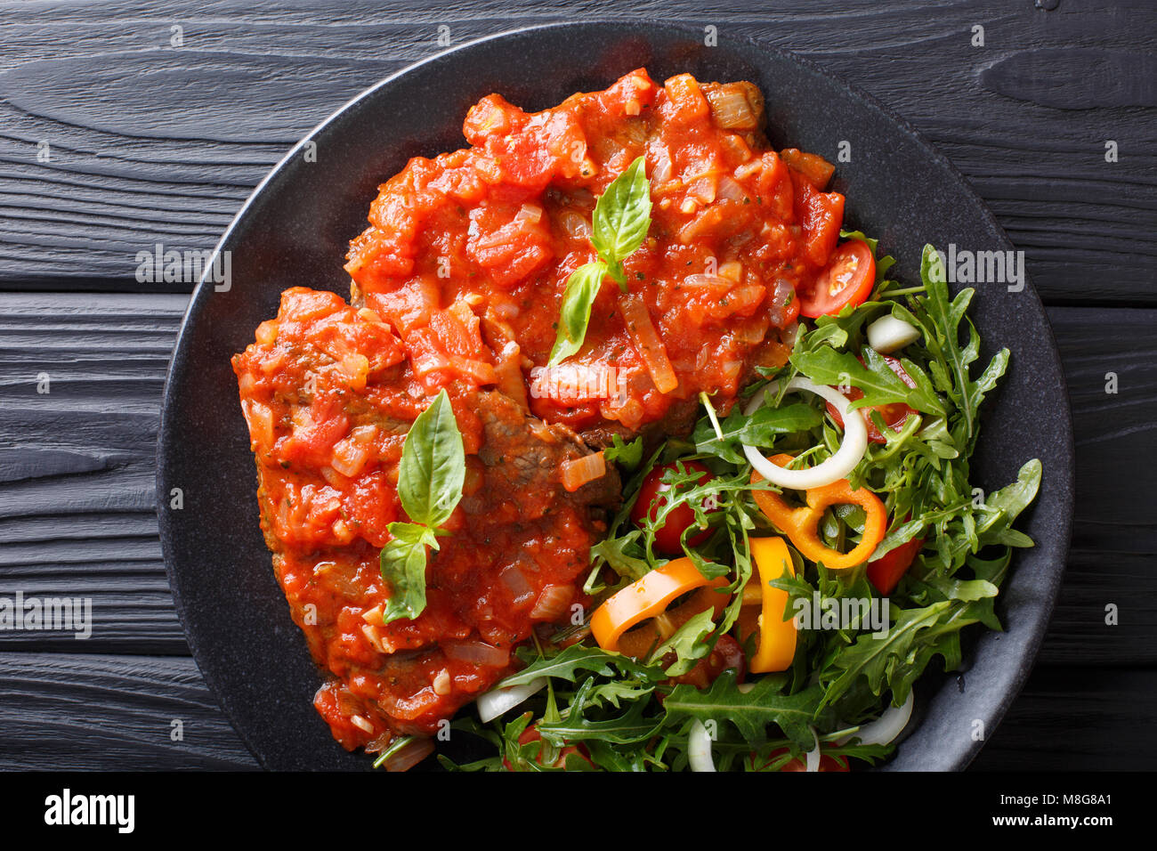 Italienische Rindfleisch Pizzaiola und frisches Gemüse Salat close-up auf einem Teller auf dem Tisch. horizontal oben Ansicht von oben Stockfoto