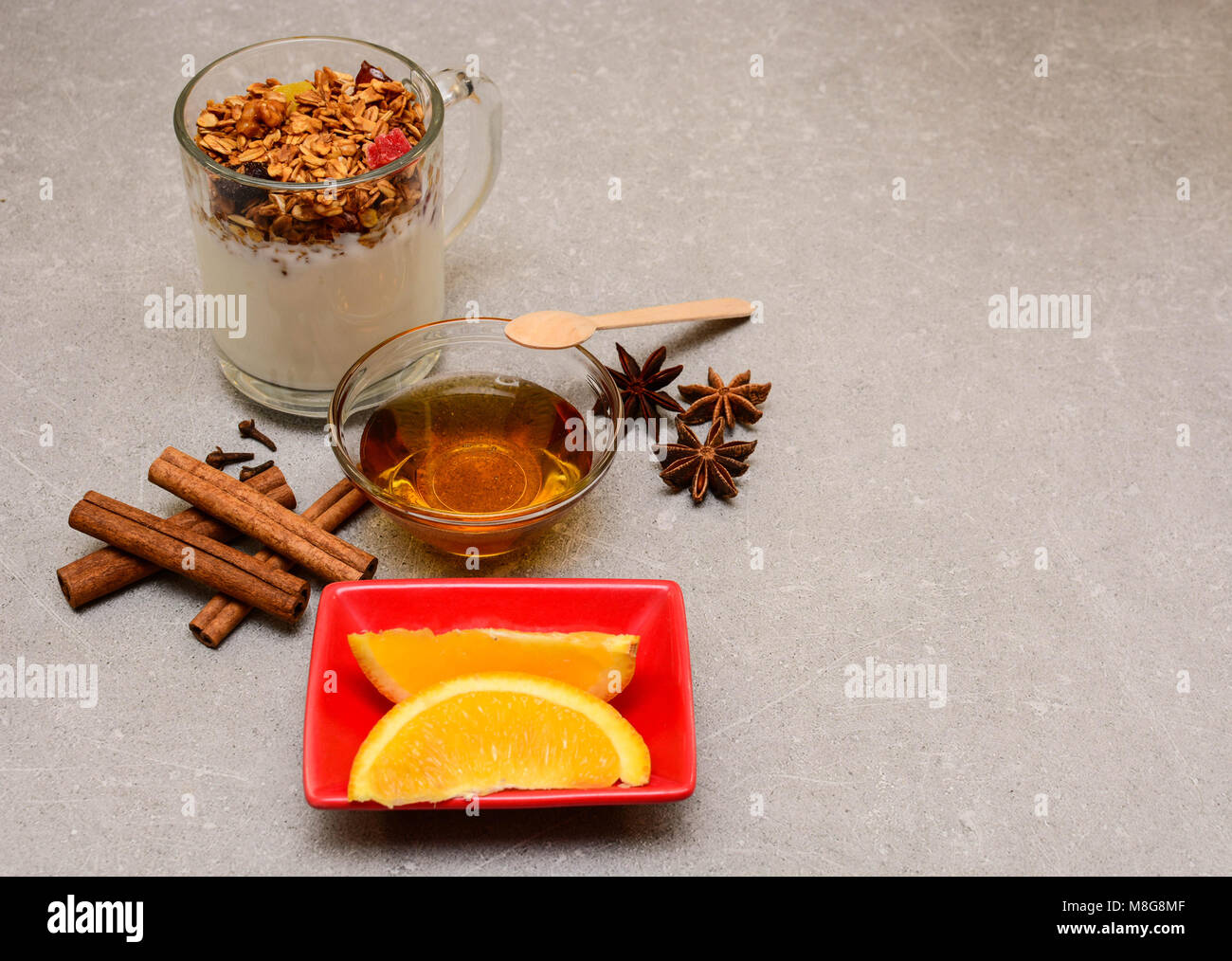 Granola mit getrockneten Beeren, kandierten Früchten, Nüssen, Joghurt, goldenem Honig, Orange, Anis, Zimtstangen und Nelken auf steinernem Hintergrund. Stockfoto