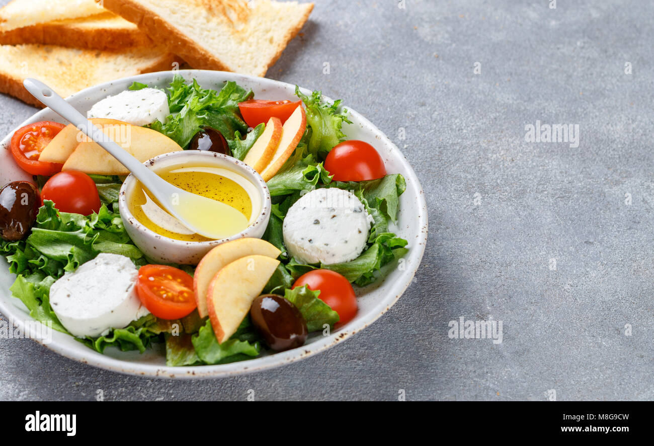 Frischen, leckeren Ziegenkäse Salat mit grünem Salat, Tomaten, Apfel, Kalamata Oliven und ein Dressing Olivenöl und geröstetem Brot Stockfoto