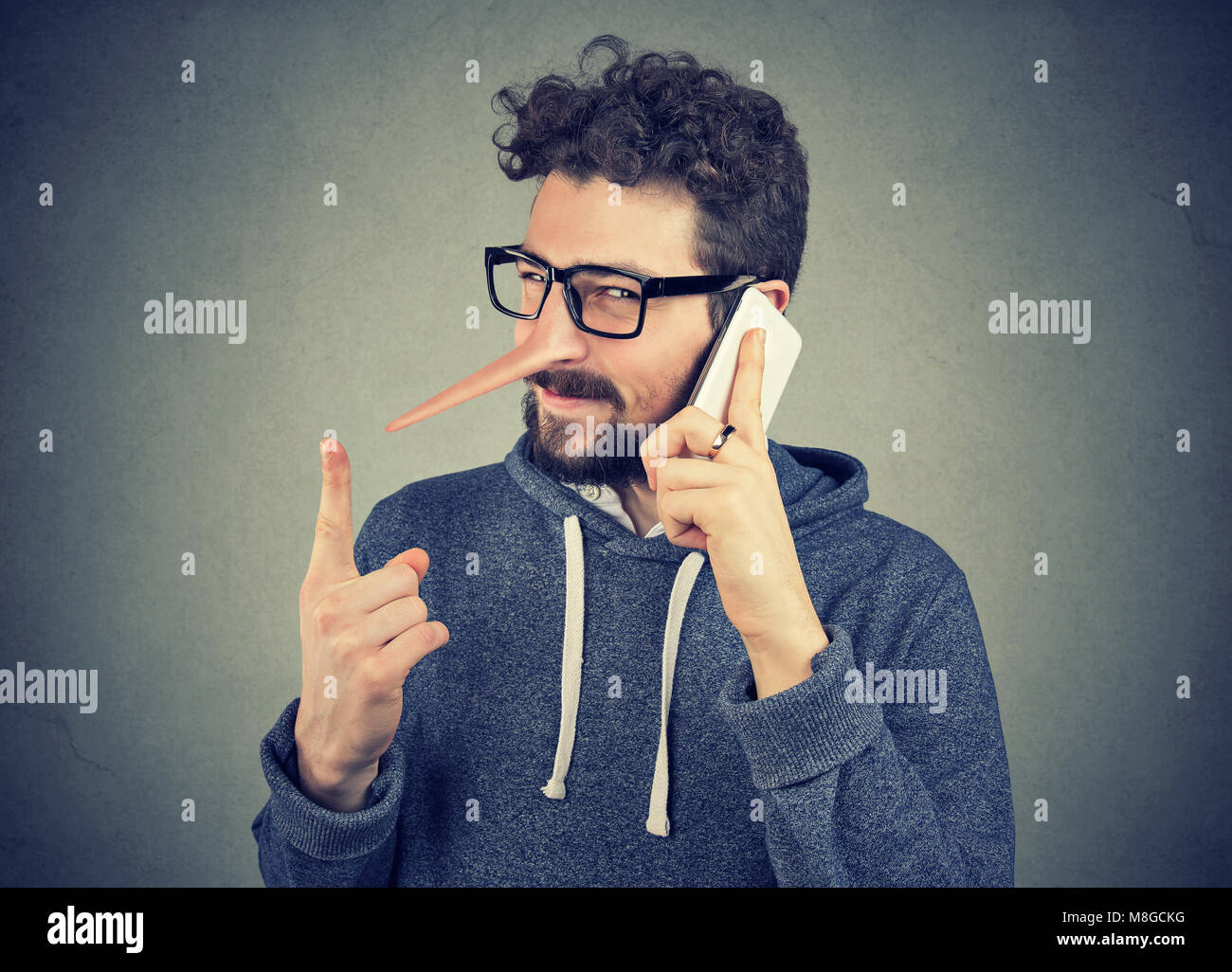 Junge sly Mann mit langen Nase Gespräch am Handy auf grauen Hintergrund. Lügner Konzept. Menschliche Emotionen Gefühle Stockfoto