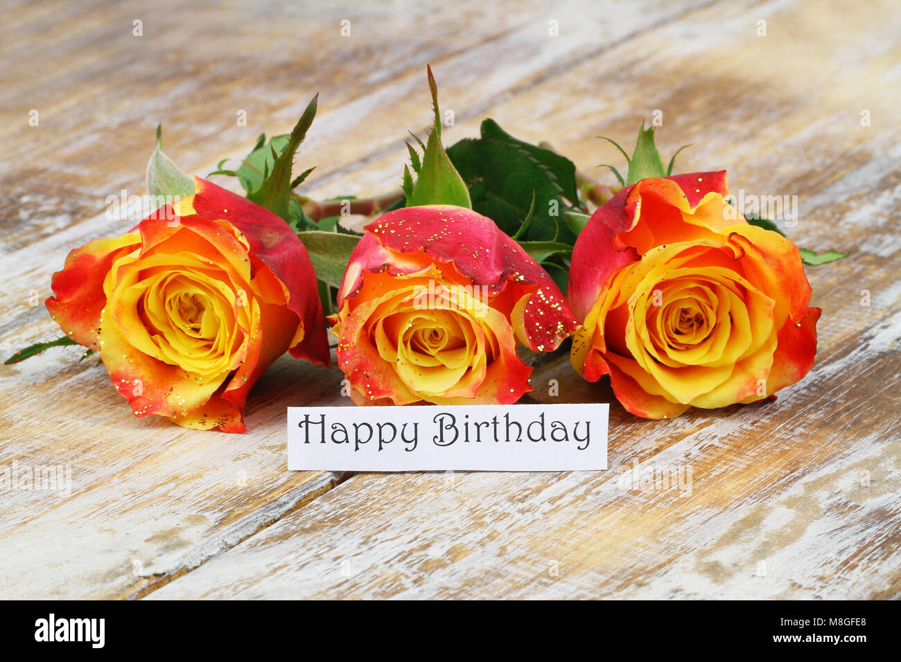 Happy Birthday Karte mit drei rote und gelbe Rosen mit Glitzer auf Holz- Oberfläche Stockfoto