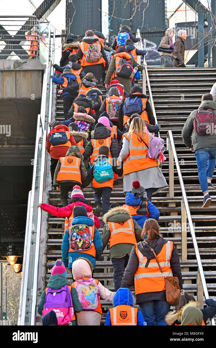 Gruppe der Grundschüler auf Klassenfahrt in der High vis Jacke oder Weste mit Lehrer und Assistenten klettern steile Stufen auf fußgängerbrücke London UK Stockfoto