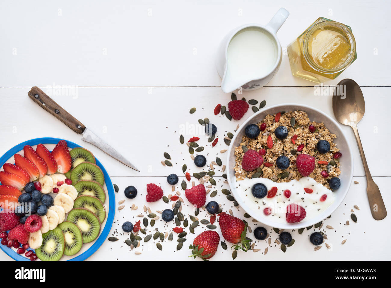 Frühstück Schüssel Müsli und einen Teller mit geschnittenem Obst mit Samen, Joghurt und Honig auf einem weißen Holz Hintergrund Stockfoto