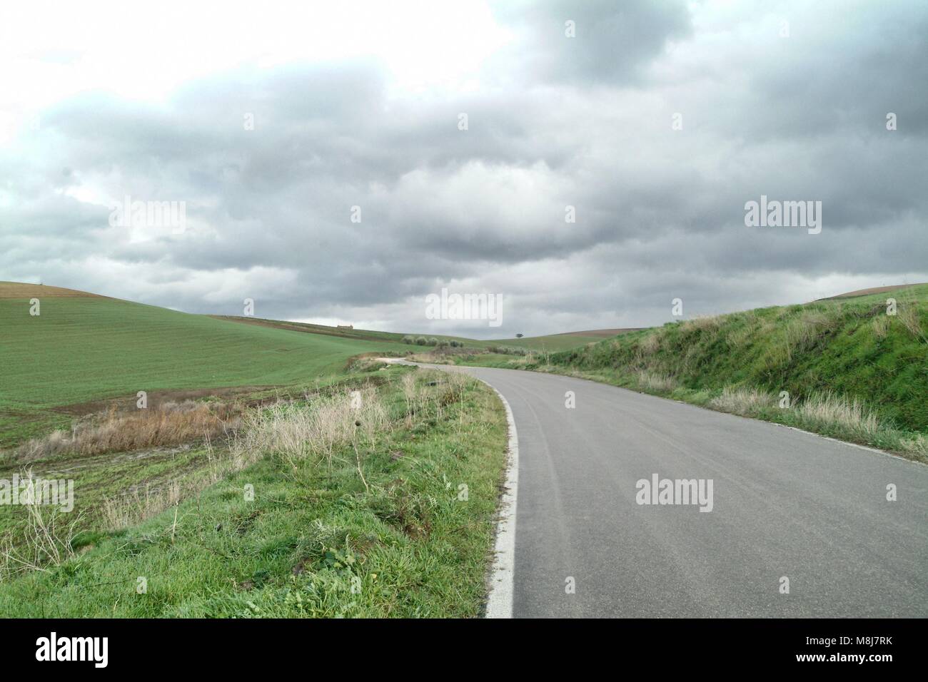 Lonely Kunst Natur Hügel auf der grünen Wiese und Asphalt unter bewölktem Himmel stürmisches Wetter Stockfoto