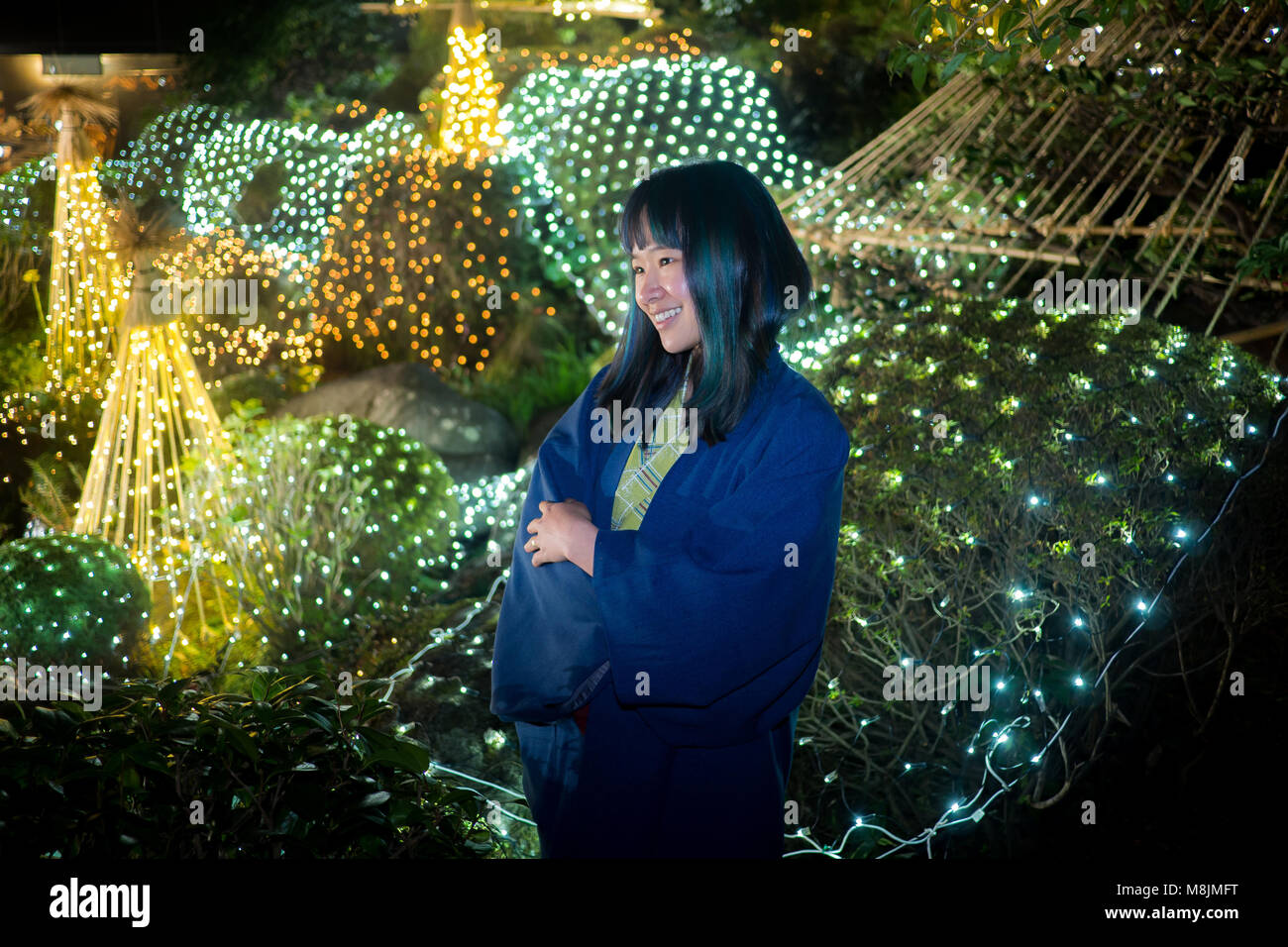 Schöne junge Frau in einer Yukata in einem japanischen Garten, die durch Leuchten posiert. Stockfoto