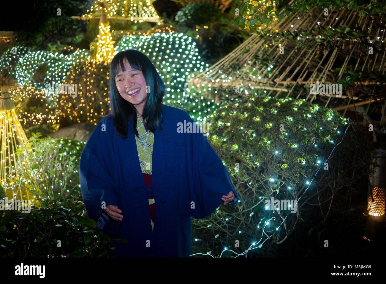 Schöne junge Frau in einer Yukata in einem japanischen Garten, die durch Leuchten posiert. Stockfoto