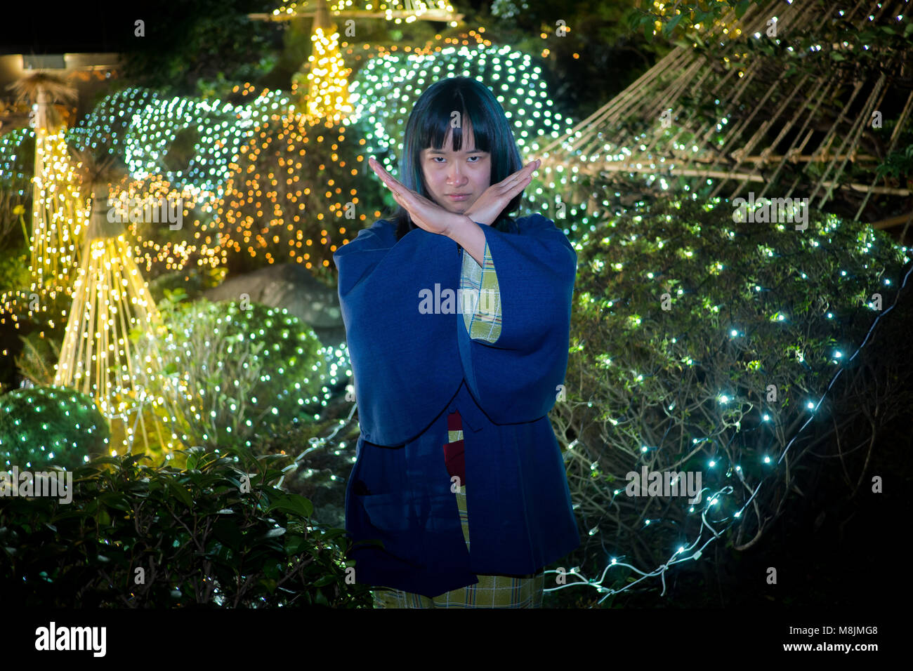 Schöne junge Frau in einer Yukata in einem japanischen Garten, die durch Leuchten posiert. Stockfoto