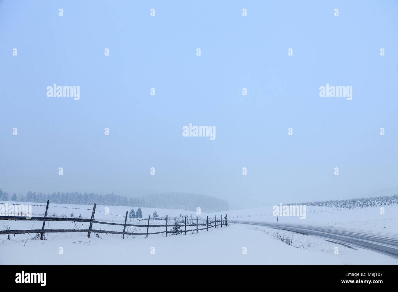 Weg bedeckt im Schnee in den bosnischen Bergen bei Sonnenuntergang, während eines schweren Winter Zustand Bild einer verlassenen Straße im Schnee im Winter fällt. Stockfoto