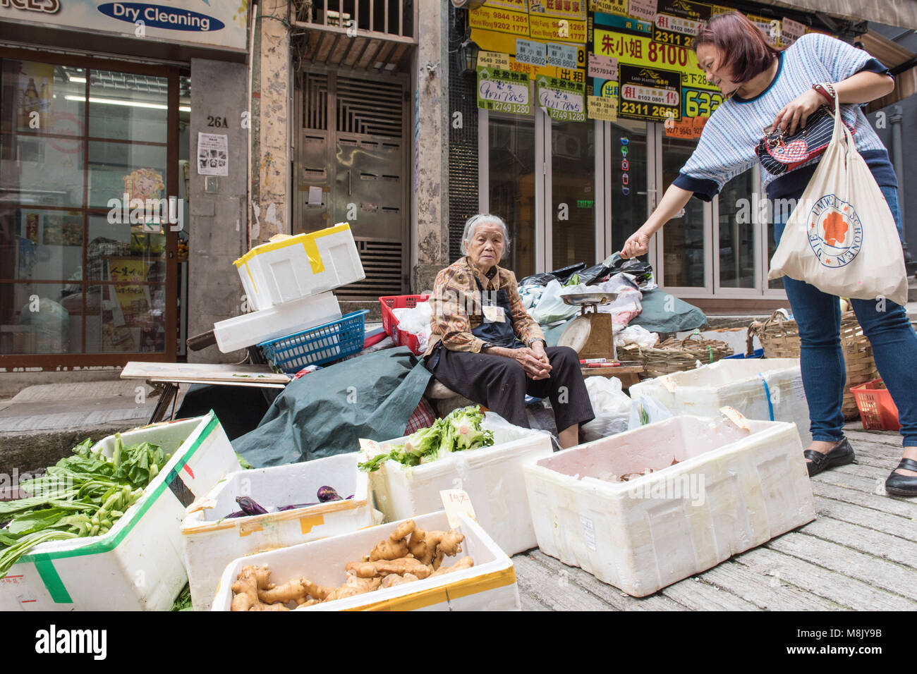 Ältere Frau Straßenhändler, lieber für die Kamera posieren als das Geld nehmen Sie von einem Kunden angeboten wird, Hongkong, China. Stockfoto