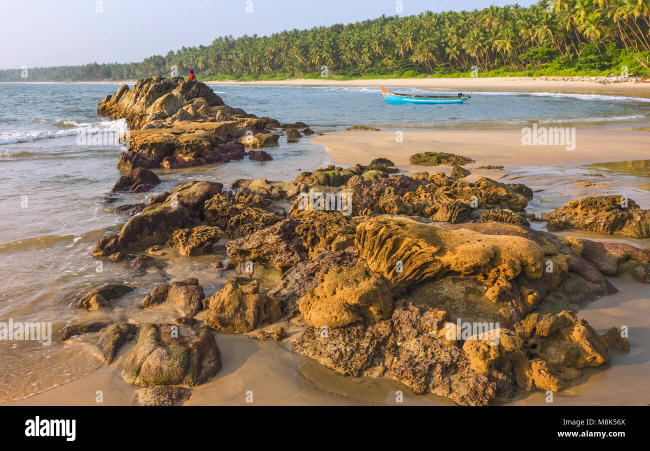 Chera Rock in der Mitte der Sandstrand mit Palmen gesäumten Strand und hölzernen Boot mit Blick auf die Arabische See bei Sonnenuntergang in der Nähe von Thottada Dorf, Srinagar, Indien. Stockfoto