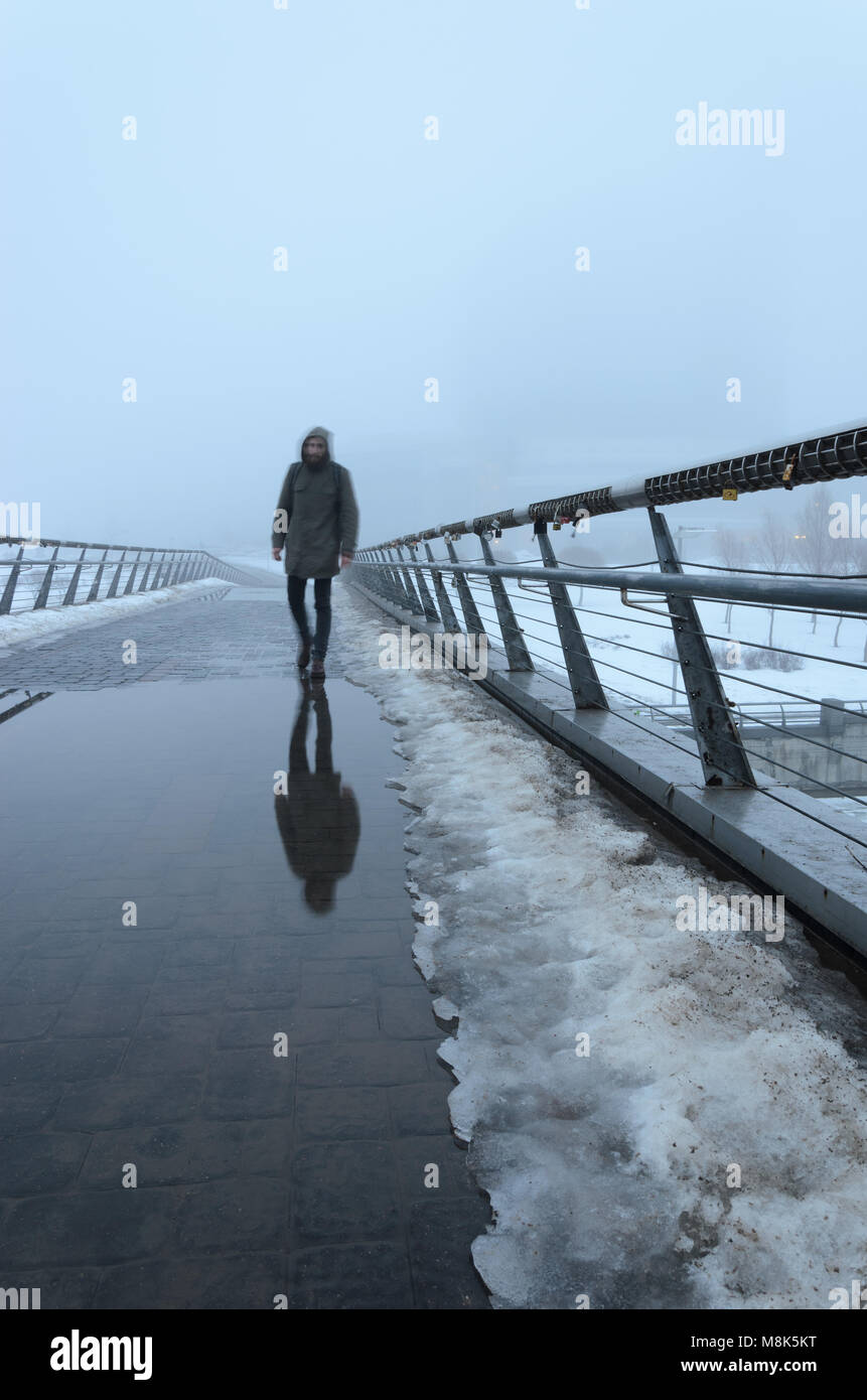 Die Silhouette eines Mannes, der durch eine Fußgängerbrücke und in Pfützen obskuren im dichten Nebel reflektiert. Mystische Hintergrund Stockfoto